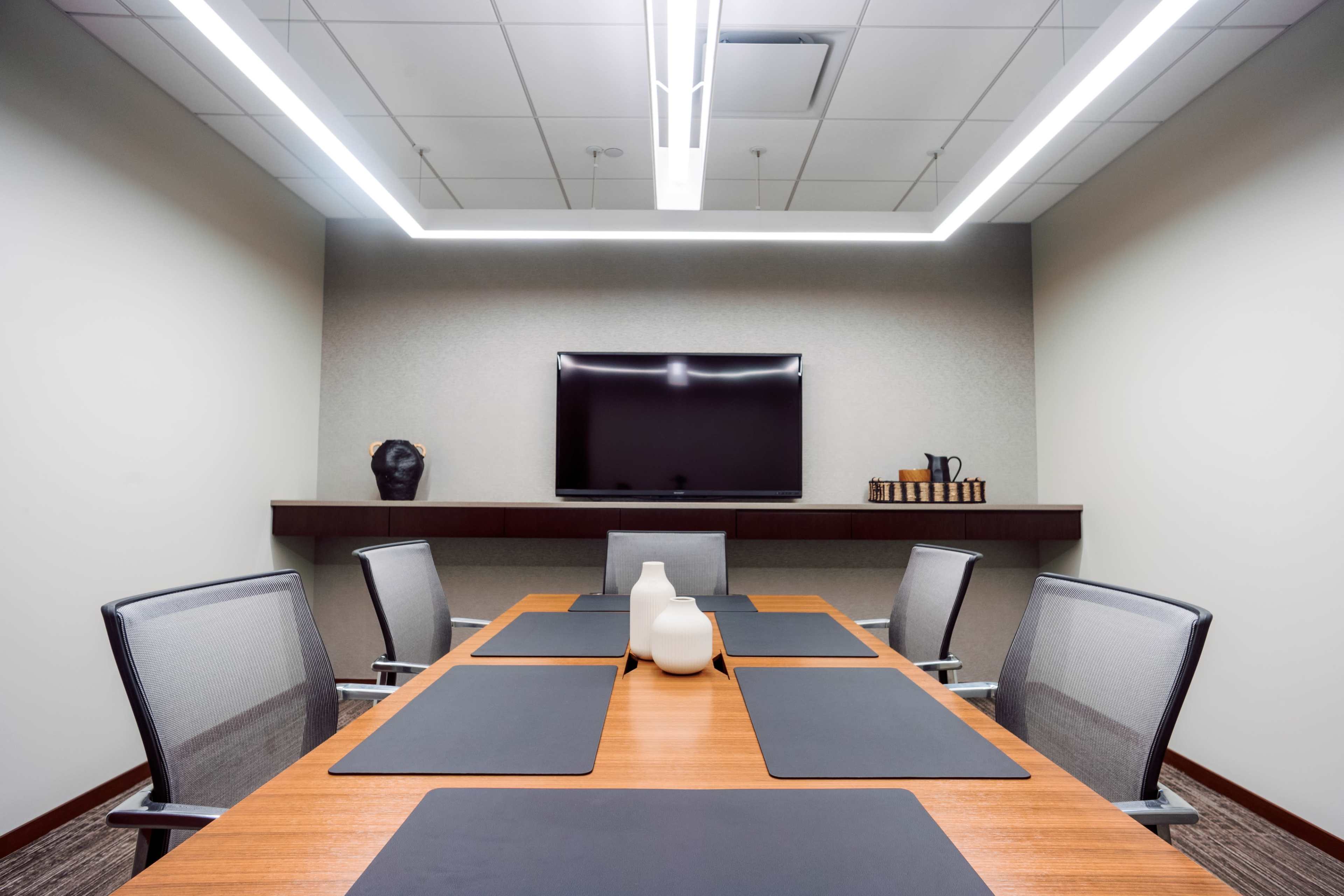 The image shows a modern conference room with a large table, six chairs, and a wall-mounted television.