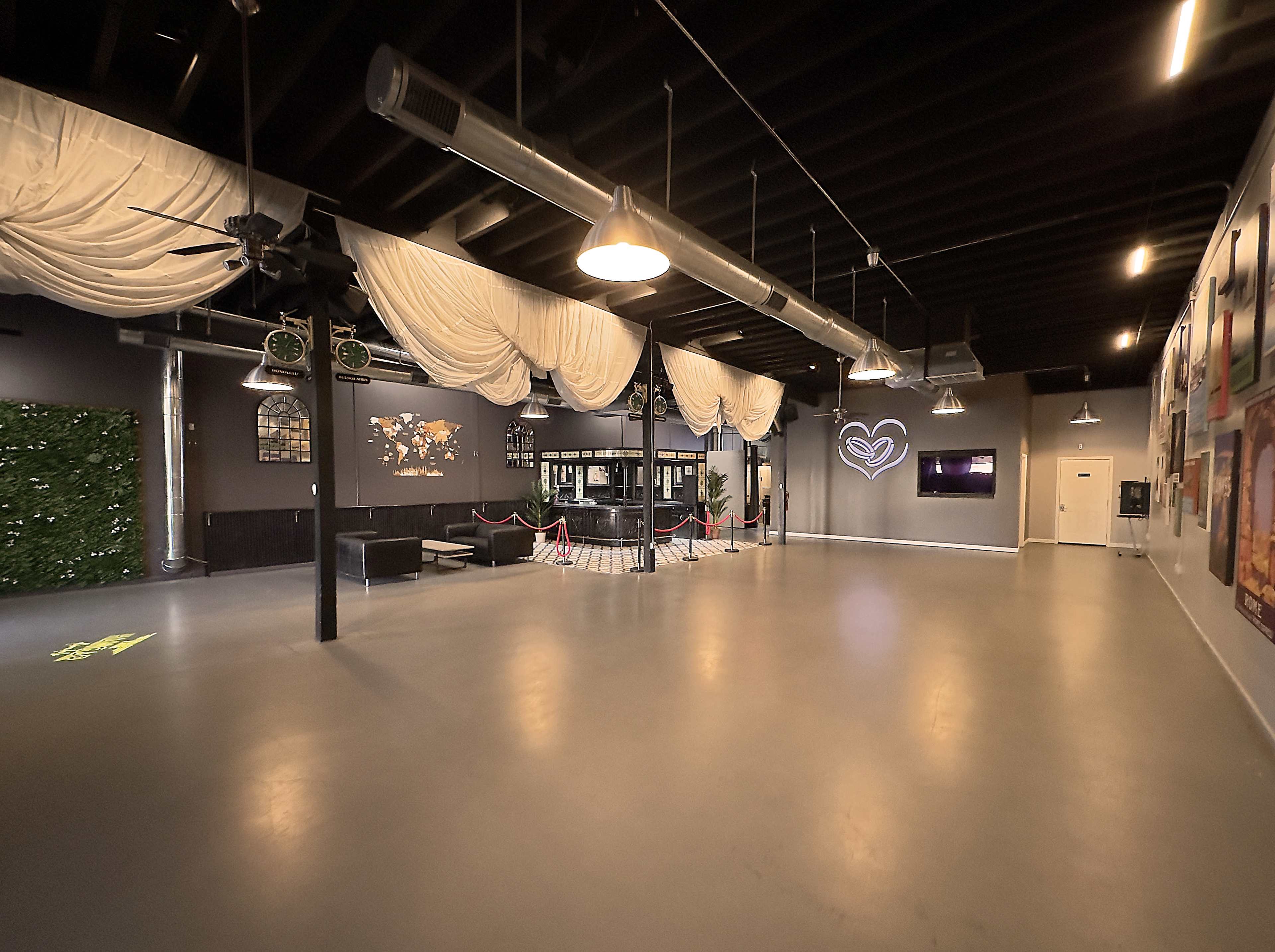 An empty event space with draped fabric overhead, exposed ceiling beams, and a small lounge area at the entrance.