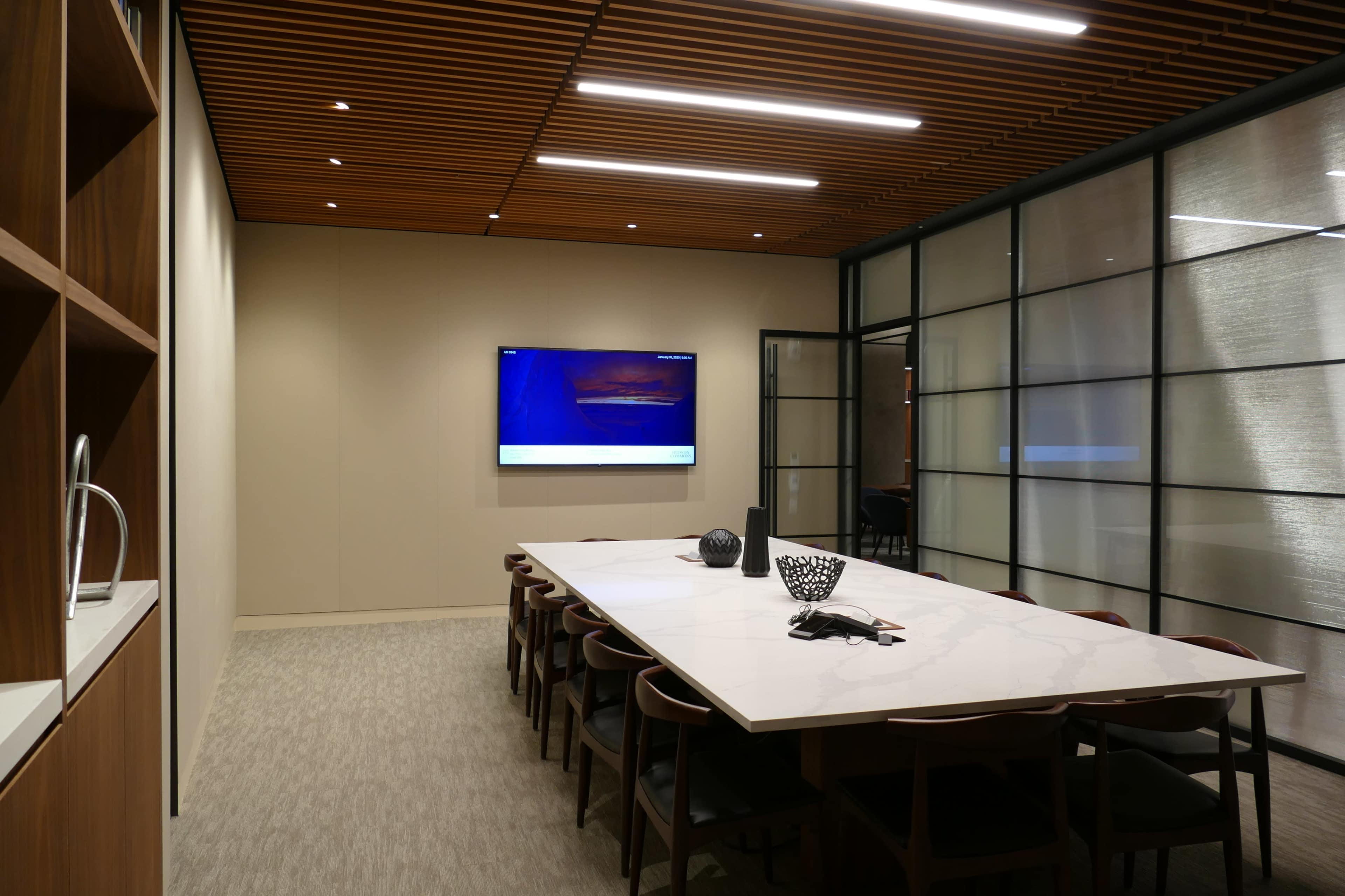A modern conference room features a large table, wall-mounted screen, and glass partitioning.