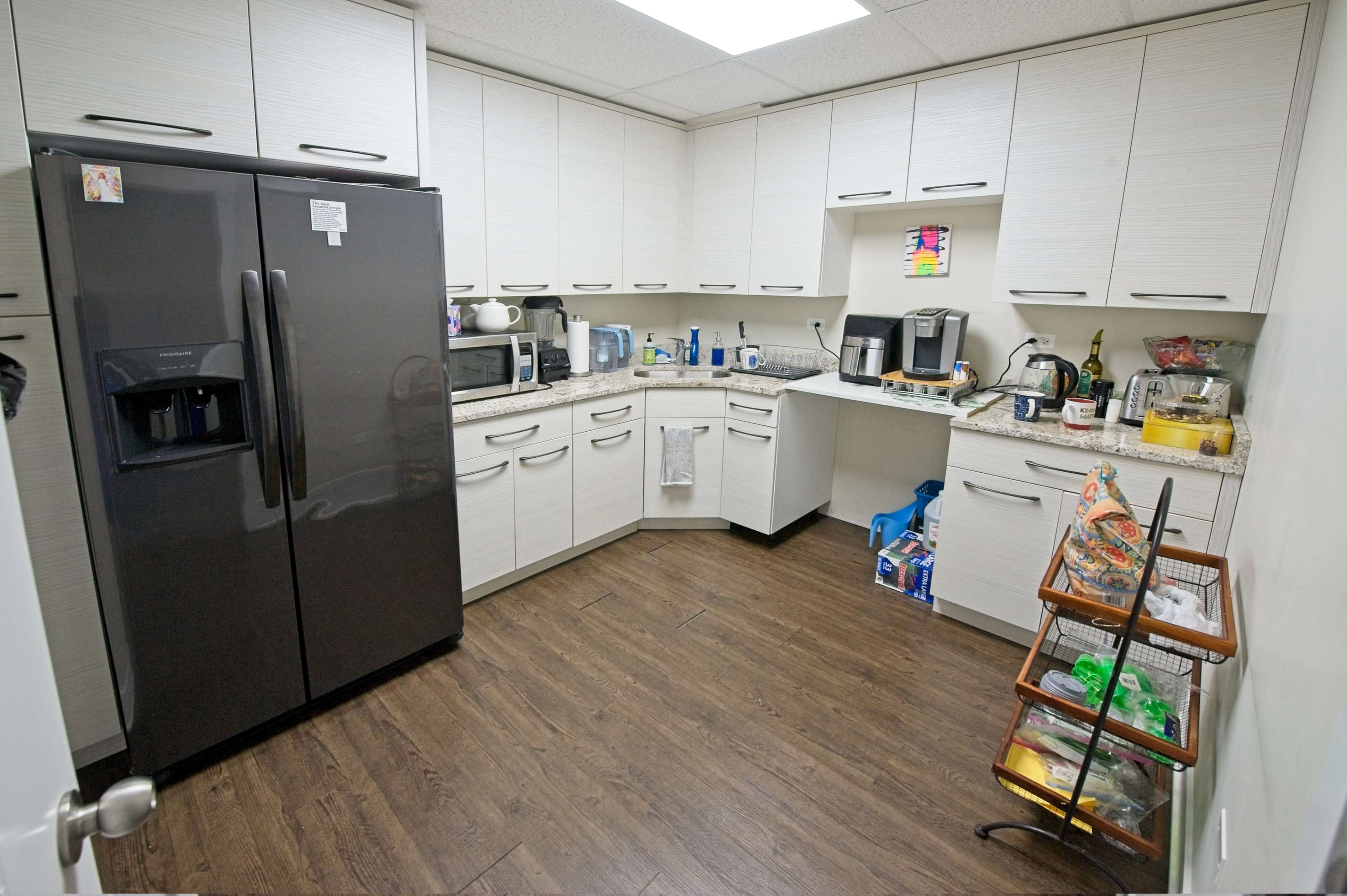 The image shows a kitchen with modern cabinets, a black refrigerator, and various appliances on the counters, including a coffee maker and microwave.