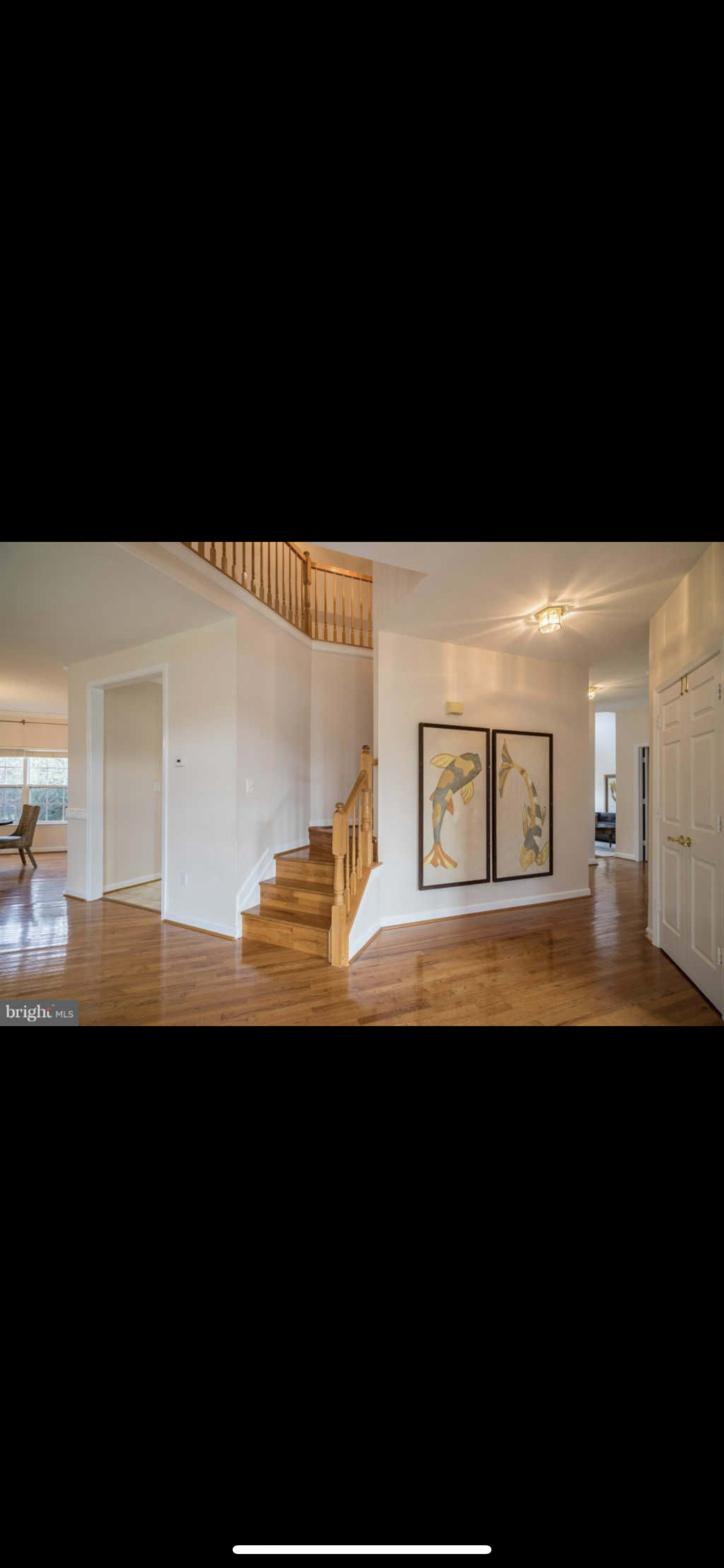 A spacious entrance hall featuring a staircase, hardwood flooring, and large framed artworks on the wall.