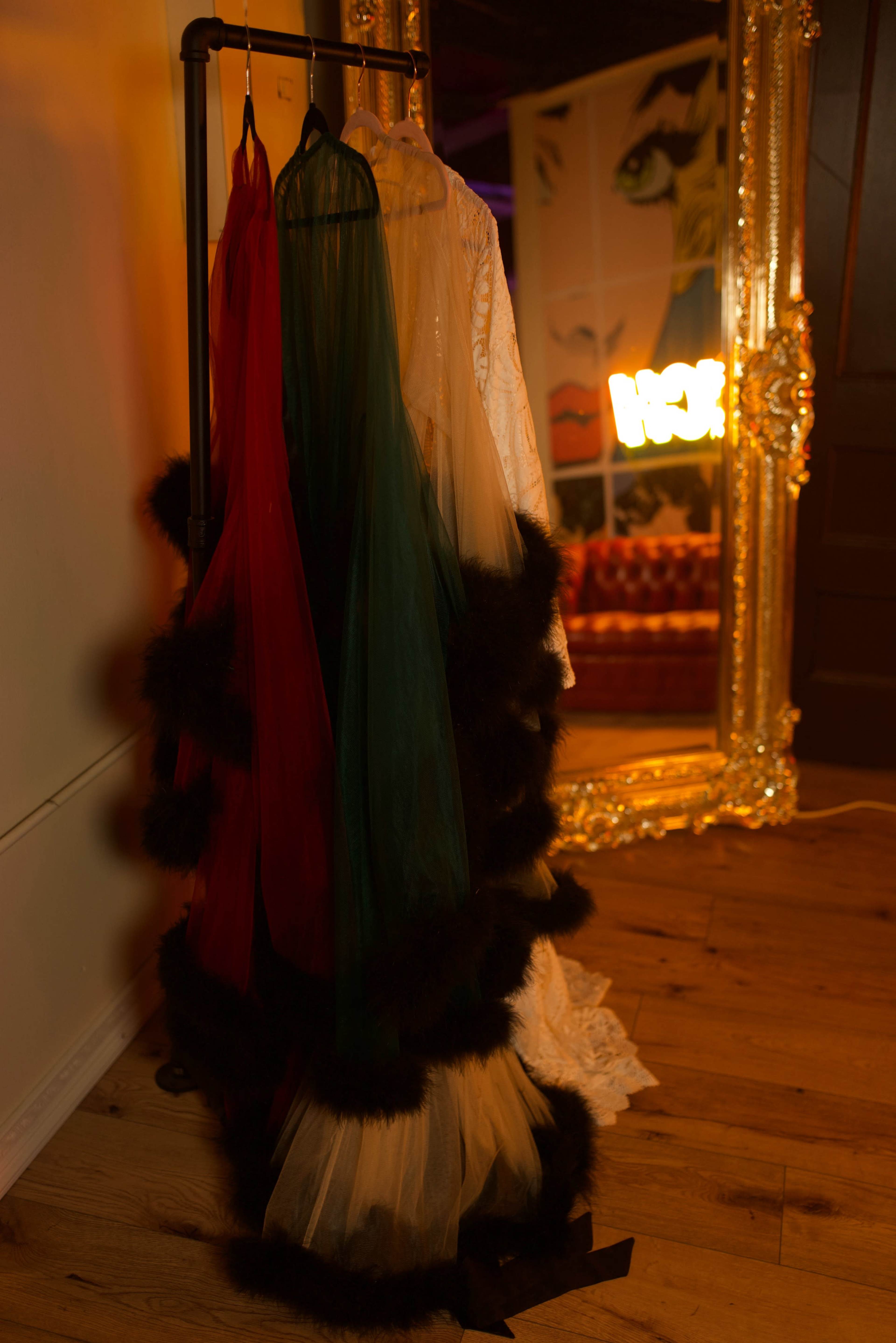 A rack holds three garments in red, green, and white, next to a large ornate mirror and a colorful illuminated sign.