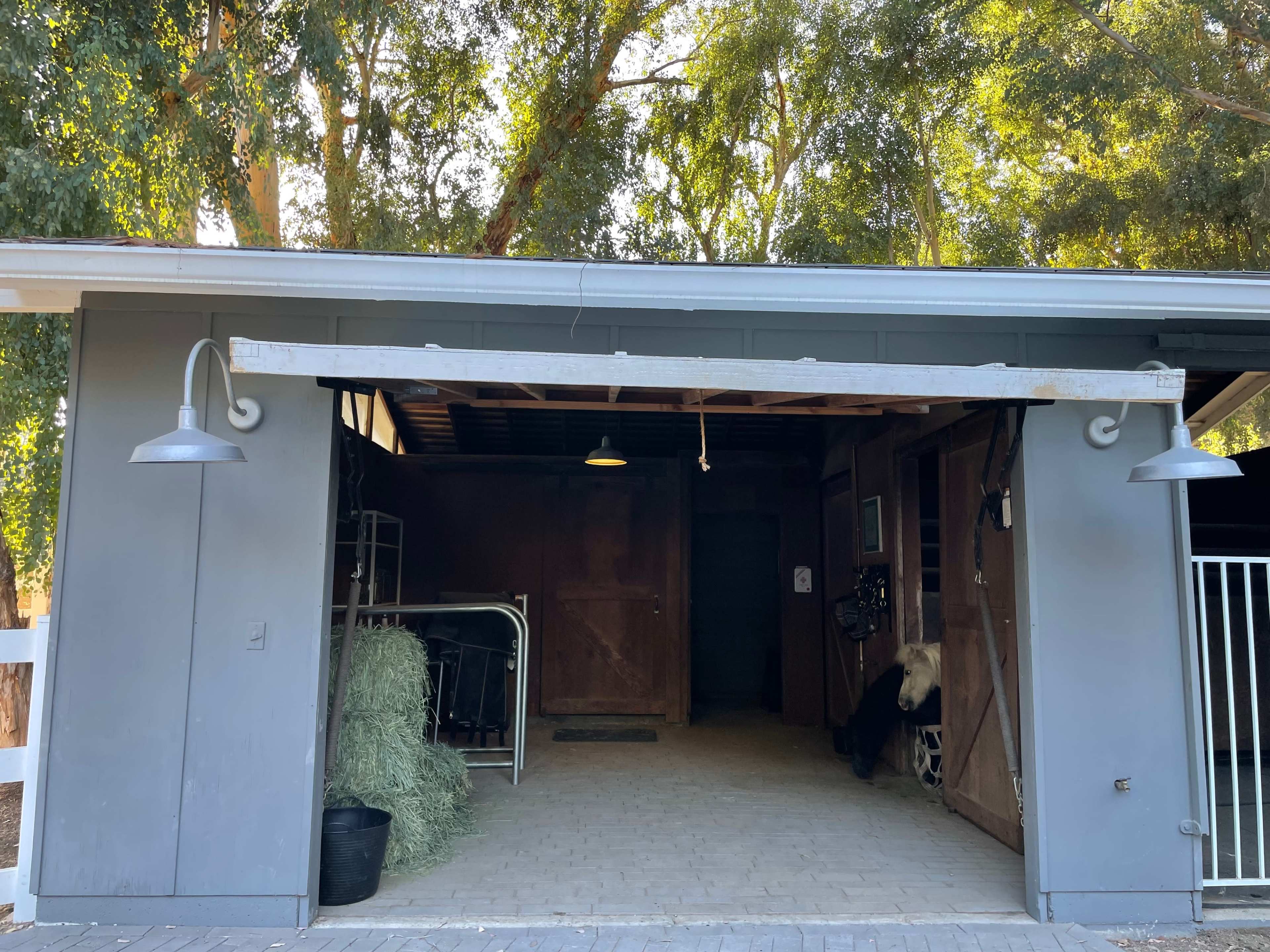 The image shows a barn with an open front, revealing a stable area that contains equipment and hay.