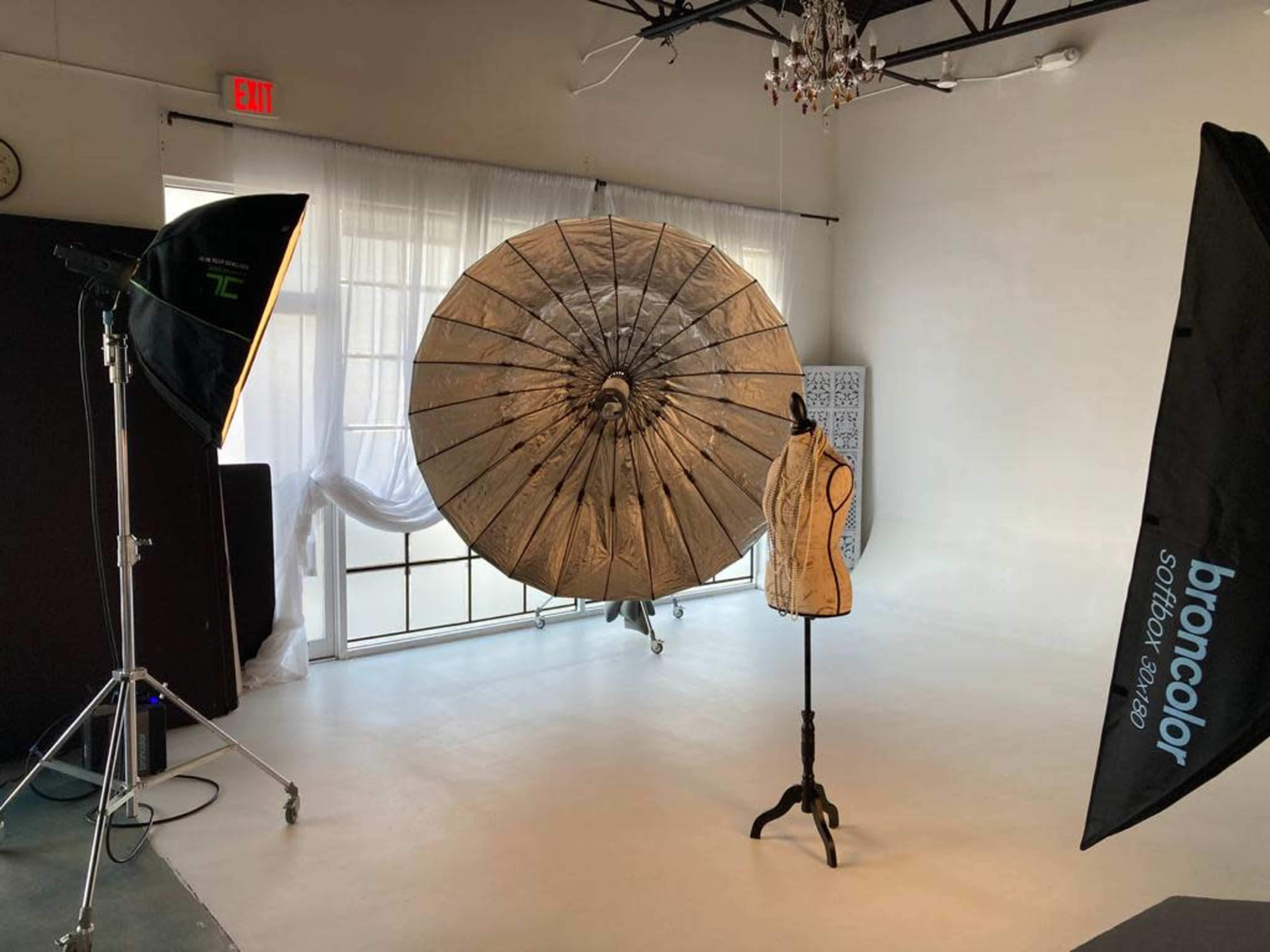 The image shows a photography studio with a large umbrella reflector, two softbox lights, and a dress form on a stand.