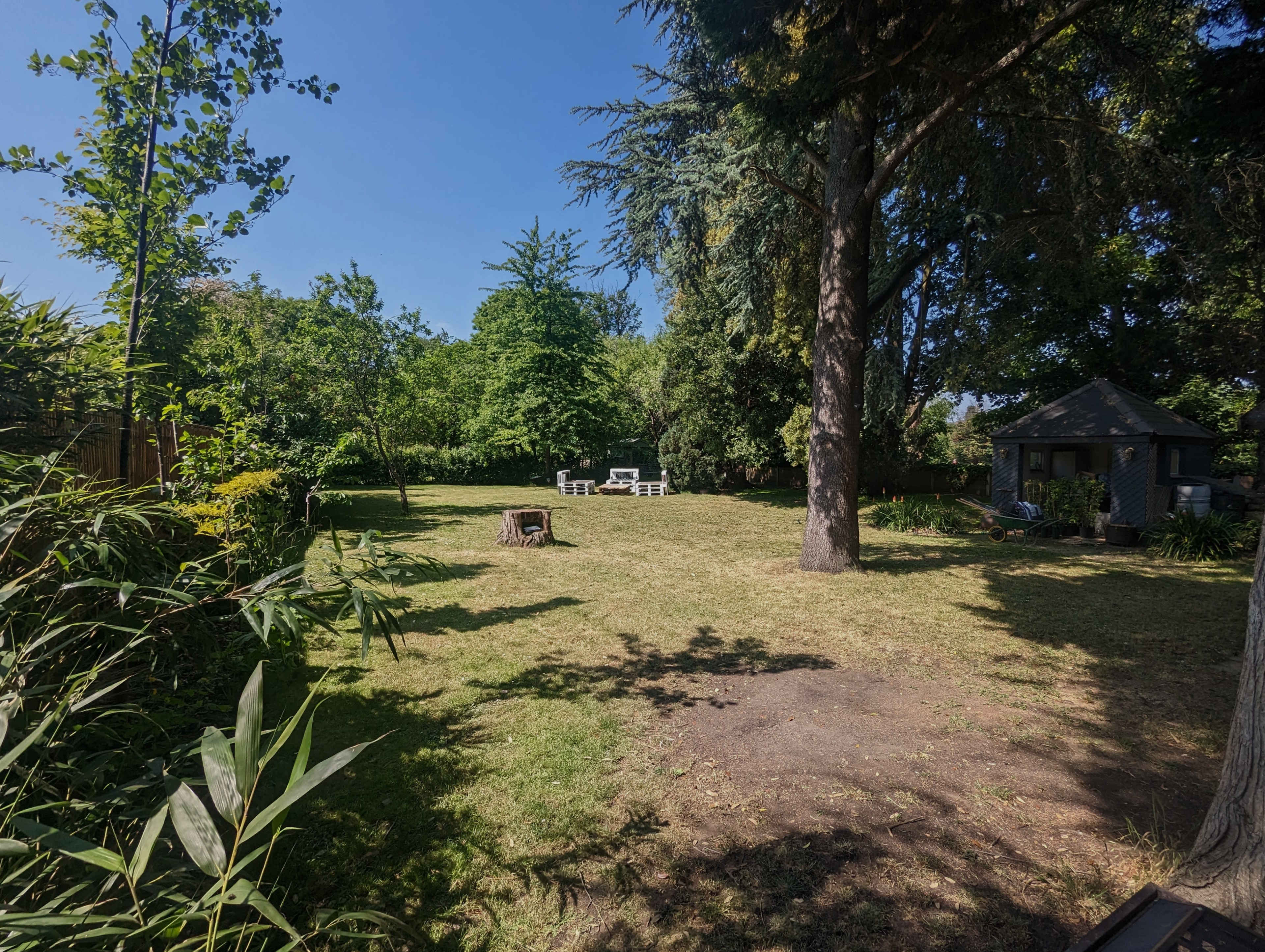A spacious garden with a manicured lawn, a fire pit, and a seating area surrounded by trees and a small shed in the background.