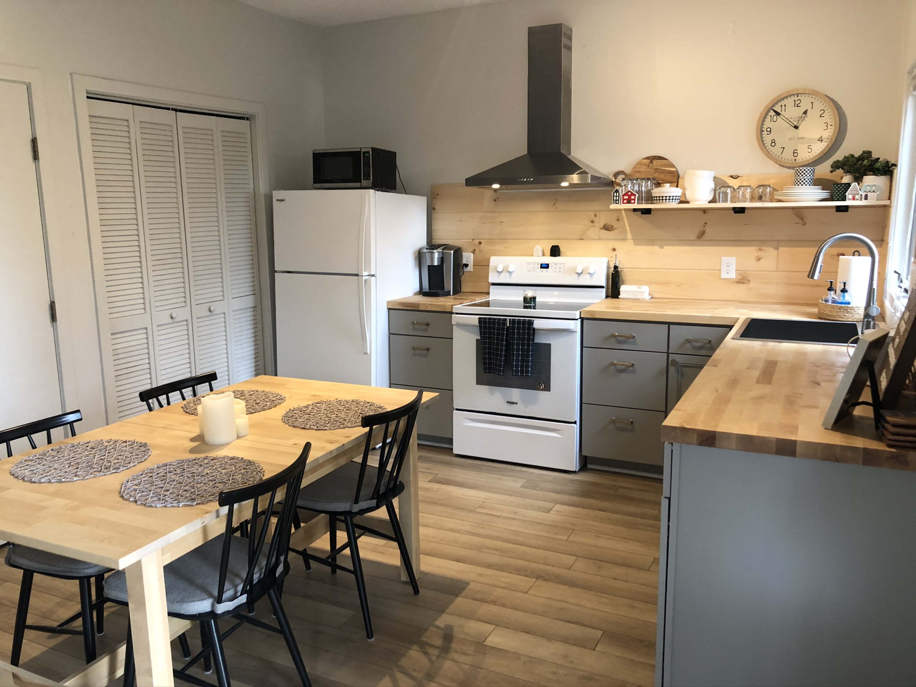 A modern kitchen with a dining table and six chairs, a white stove, a refrigerator, and wooden shelves displaying various kitchen items.