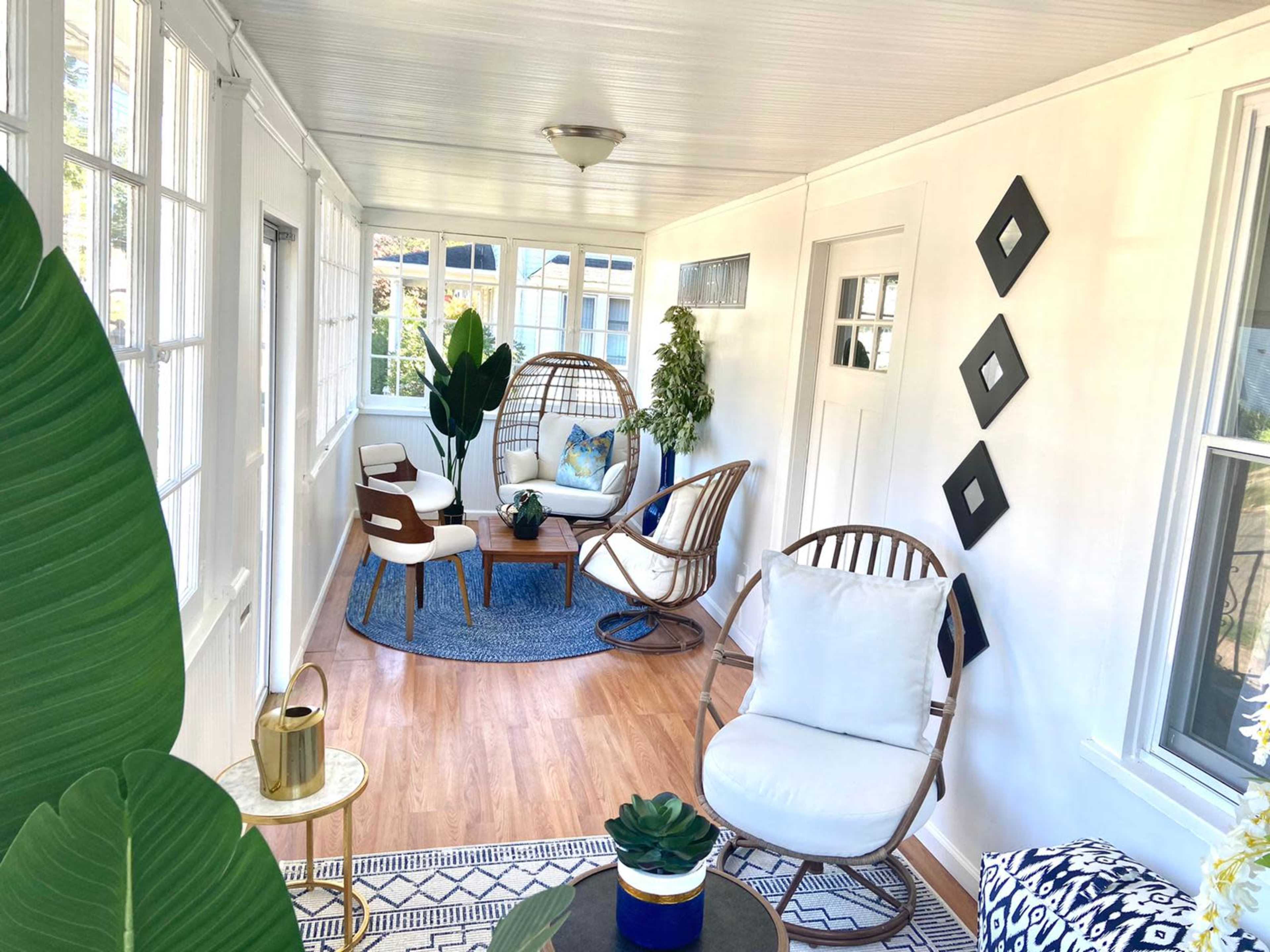 A bright sunroom with seating arrangements, plants, and decorative elements on the walls and furniture.
