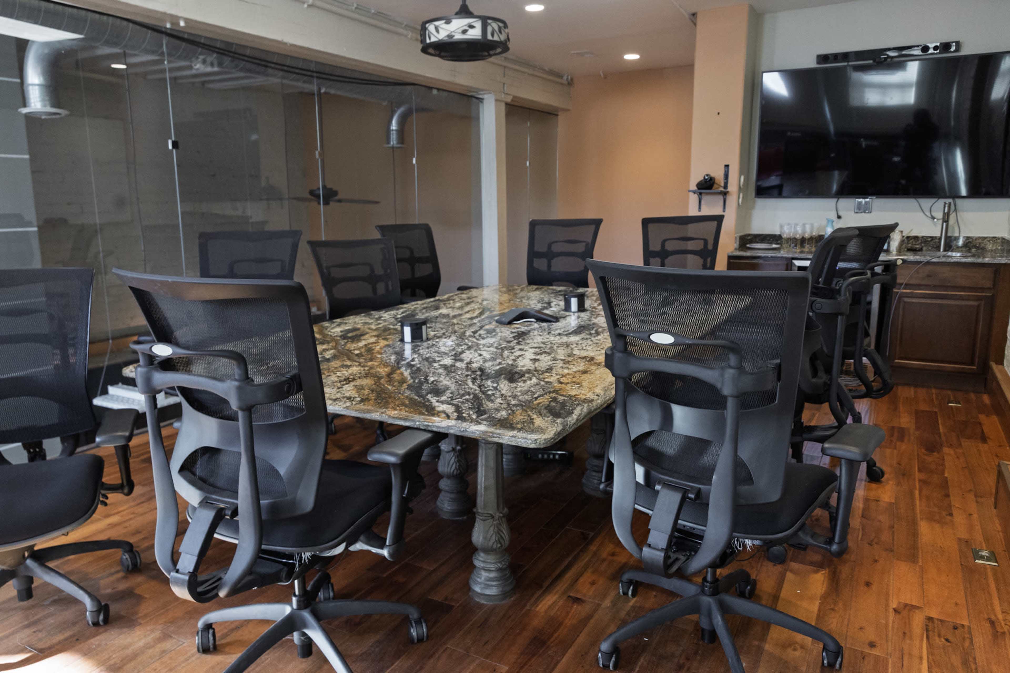 A conference room features a large, granite-topped table surrounded by ergonomic office chairs and equipped with modern audiovisual technology.