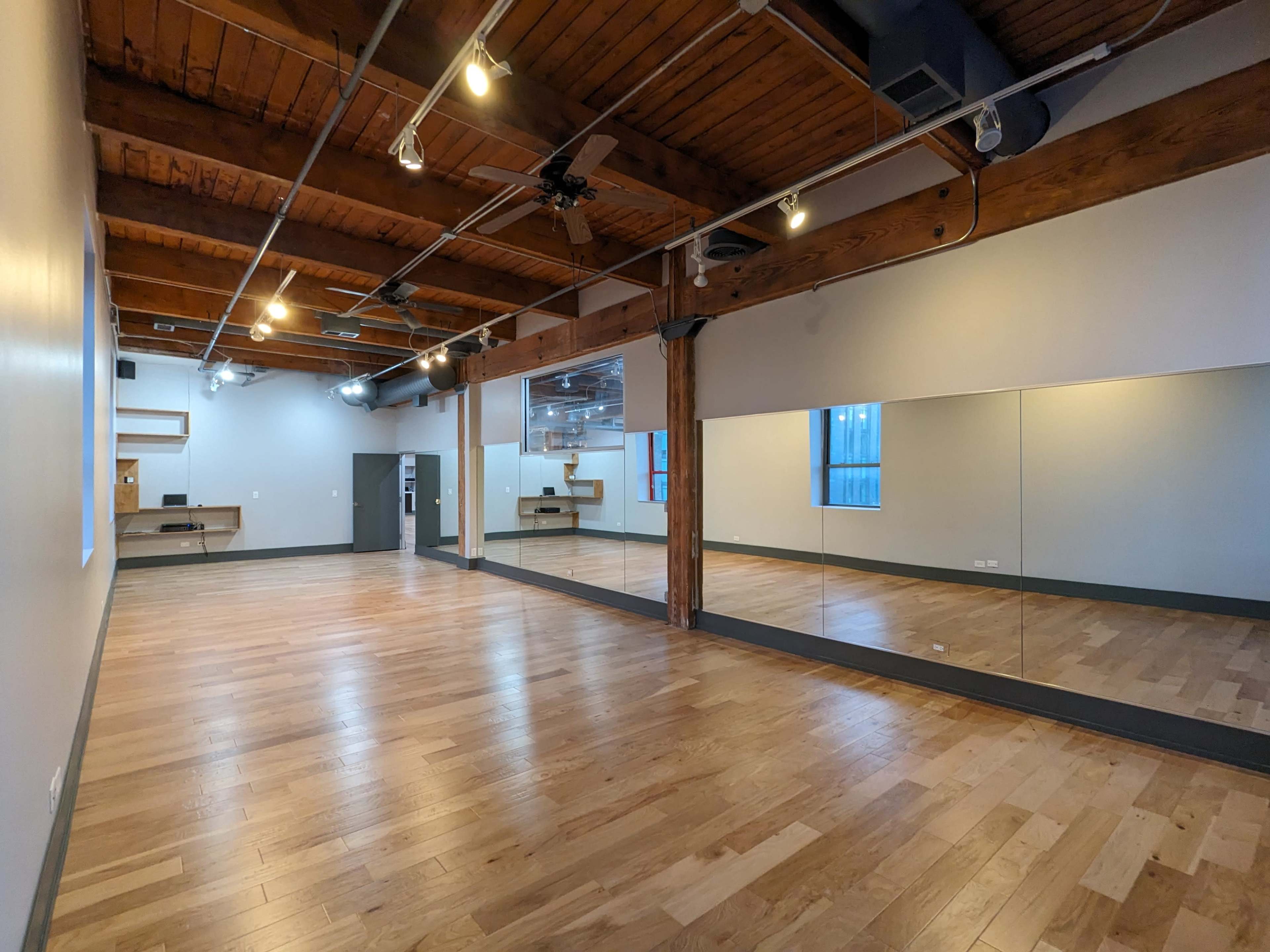 A spacious room with wooden floors, exposed beams, and large mirrors along one wall.