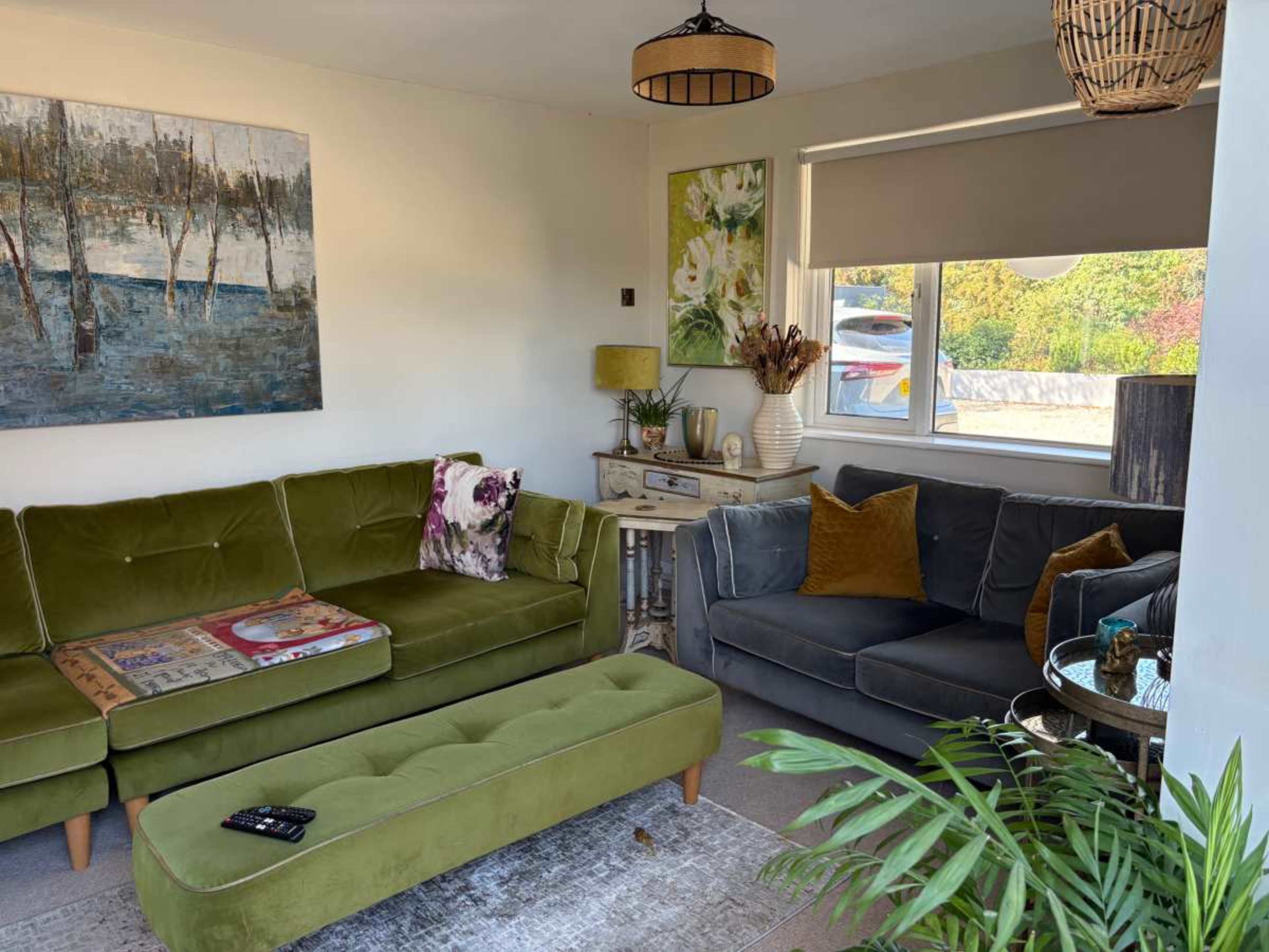 The living room features a green velvet sofa, a dark gray couch, a painted artwork on the wall, and a coffee table surrounded by decorative plants.