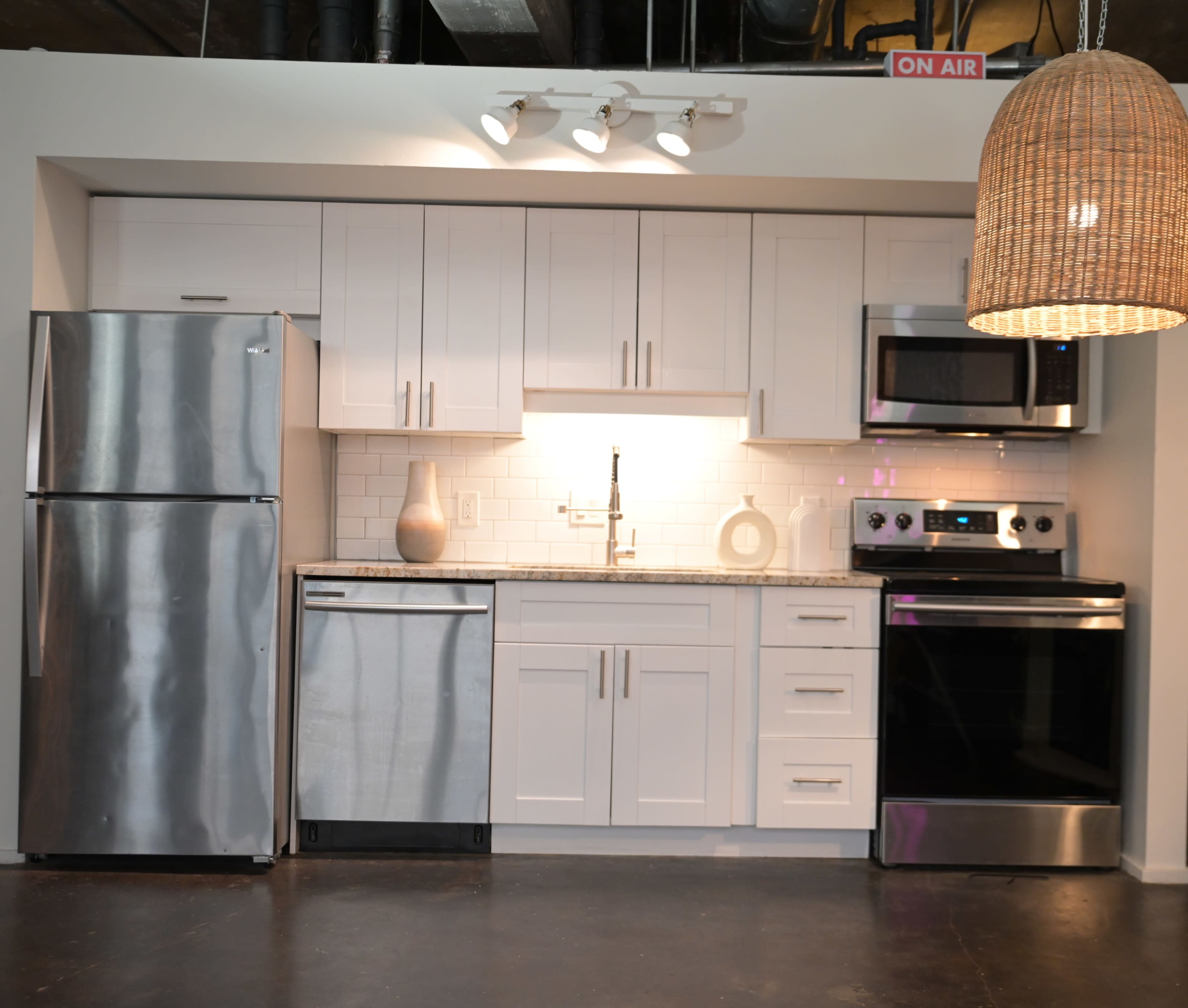 The image shows a modern kitchen with stainless steel appliances, white cabinetry, and a granite countertop.