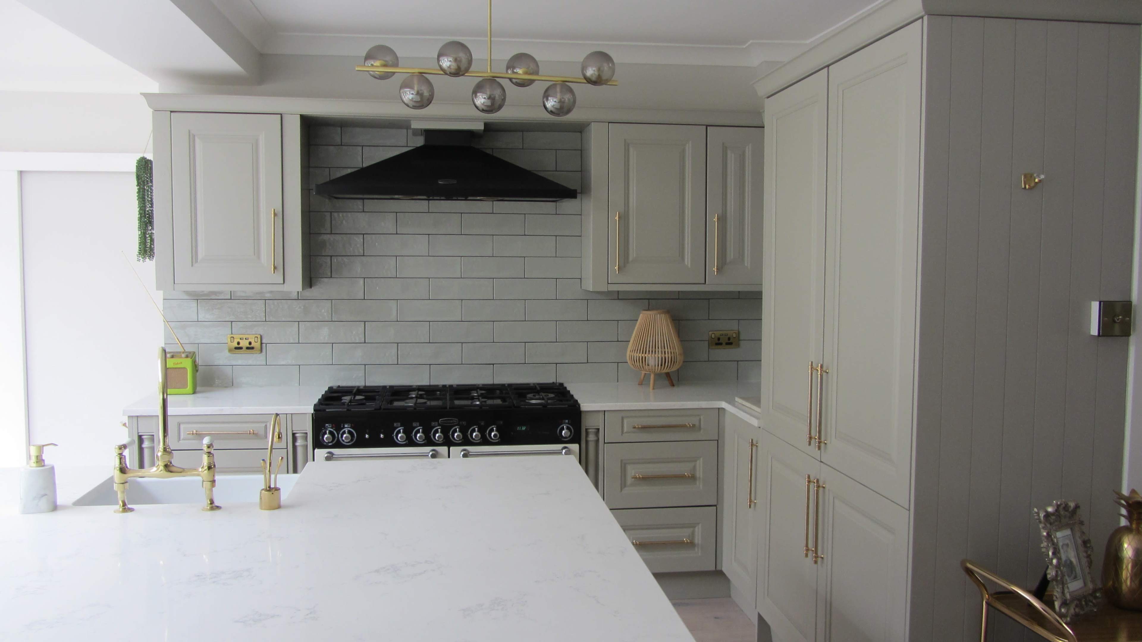 The image shows a modern kitchen featuring light gray cabinetry, a black gas stove, a quartz island, and a pendant light fixture with round bulbs.