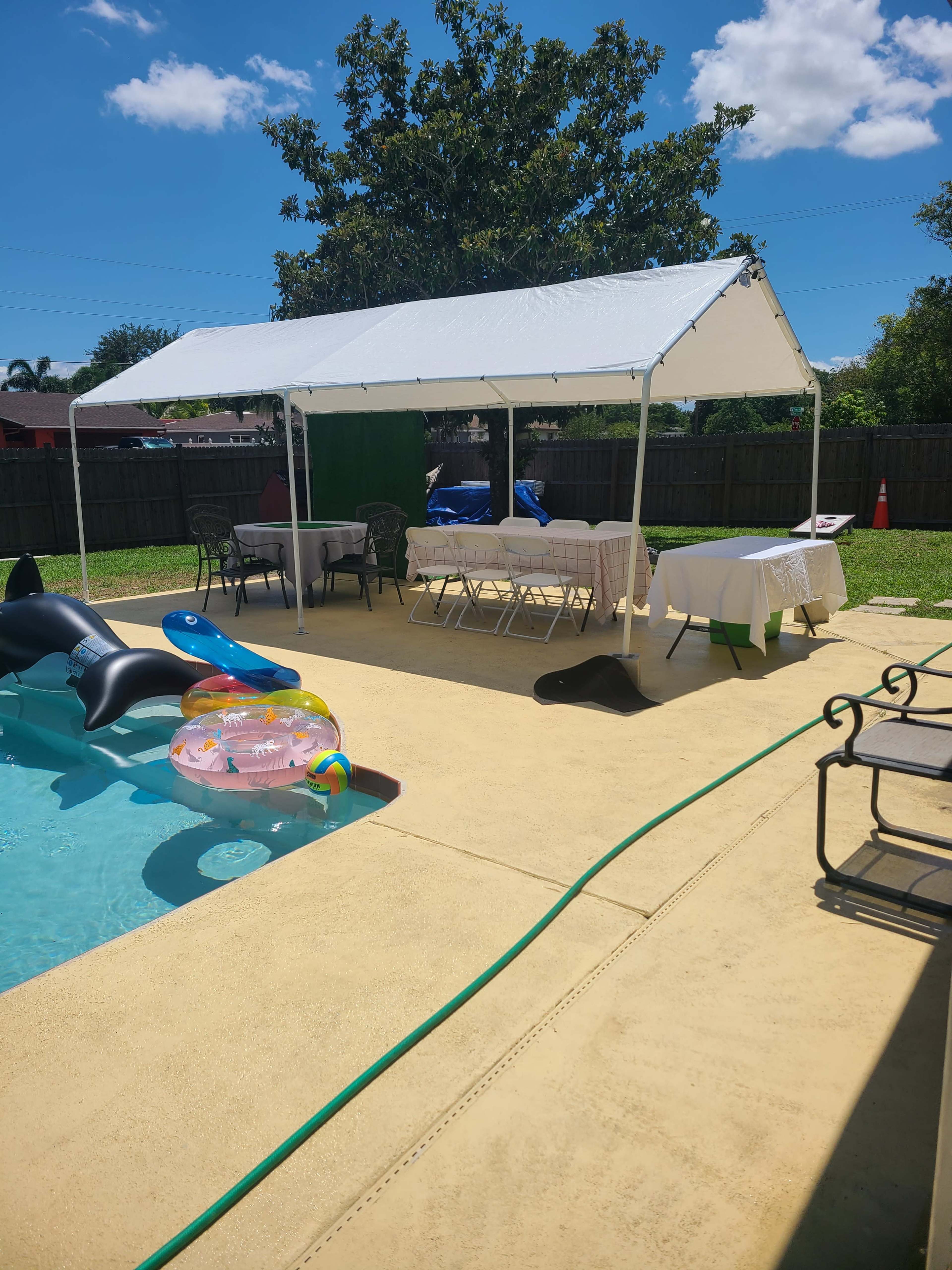 A shaded canopy setup next to a swimming pool features tables and chairs arranged for an outdoor gathering.