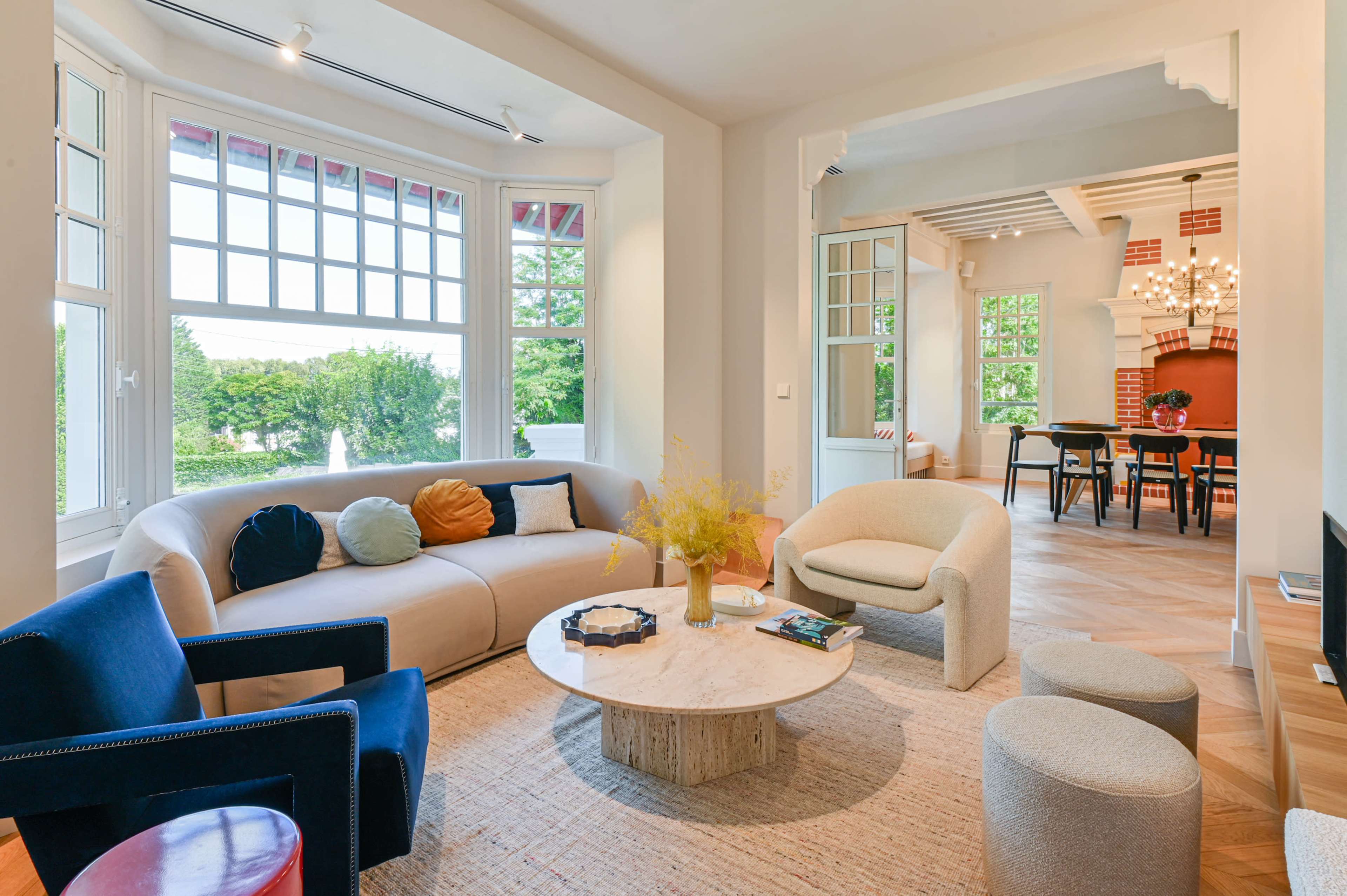 The image shows a modern living room with a curved sofa, a round coffee table, and large windows allowing natural light to fill the space.