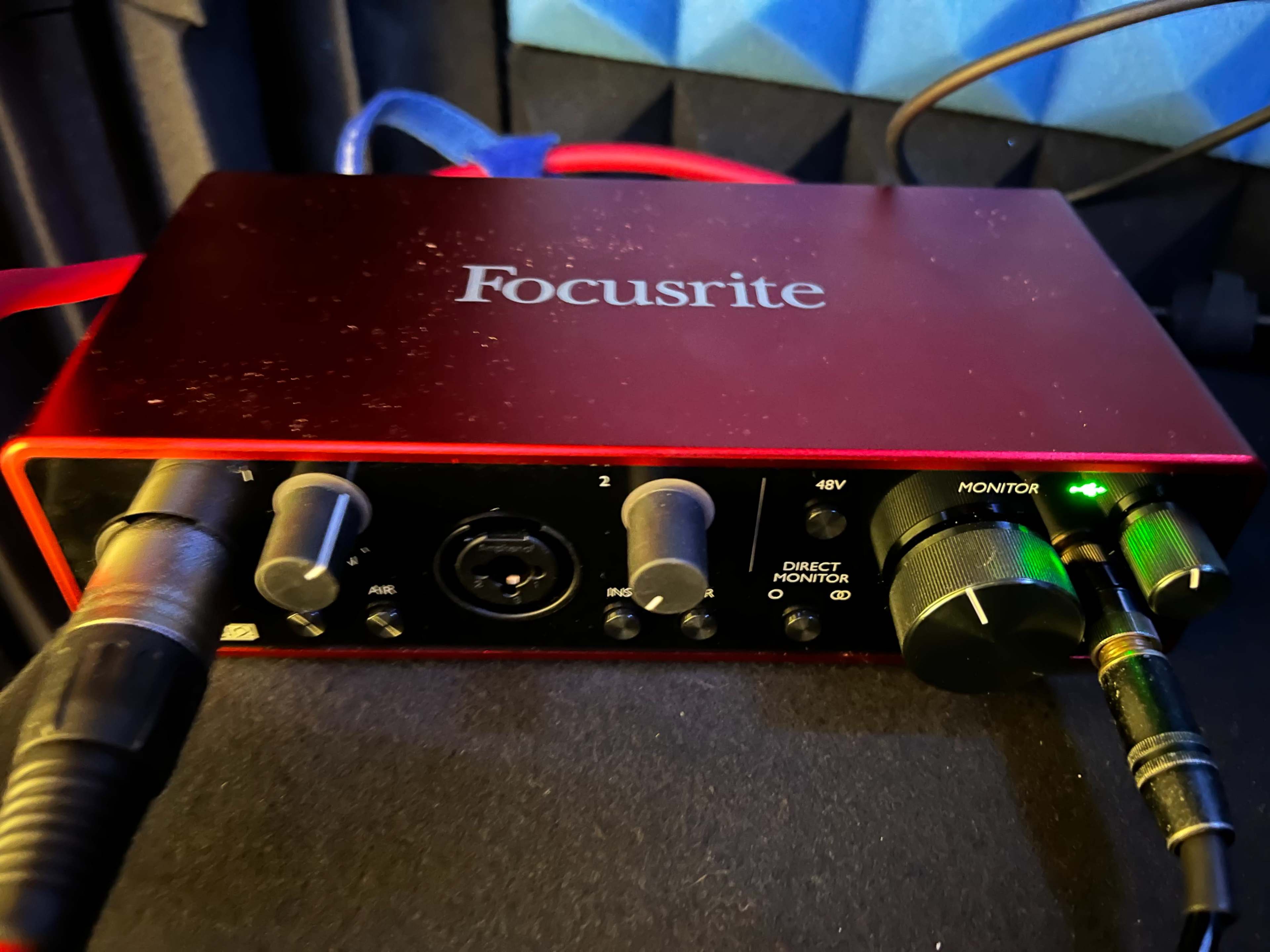 A red Focusrite audio interface with various input and output knobs, cables connected, and LED indicators.