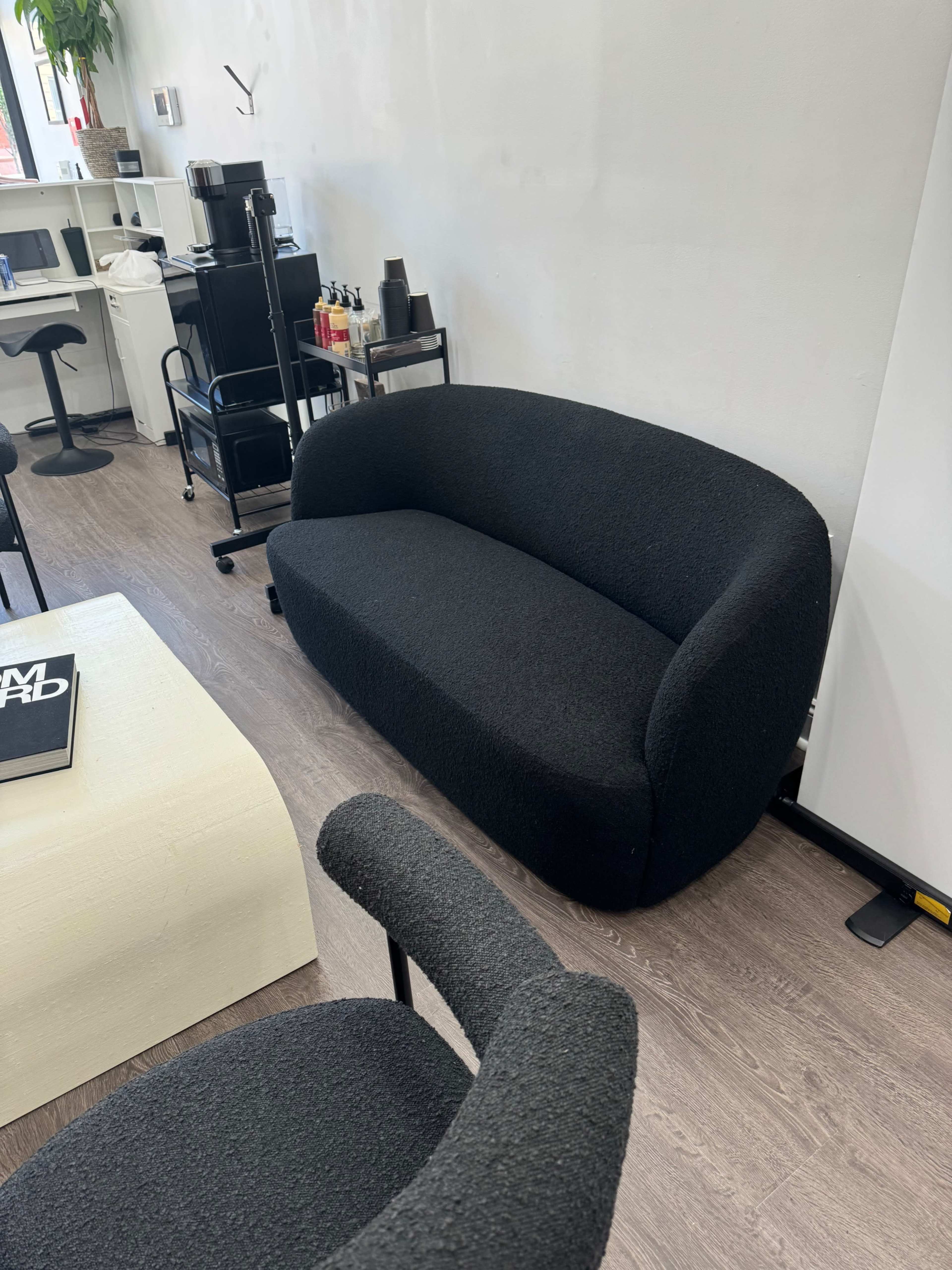 A black, curved sofa placed in a modern interior space with light-colored walls and wooden flooring.