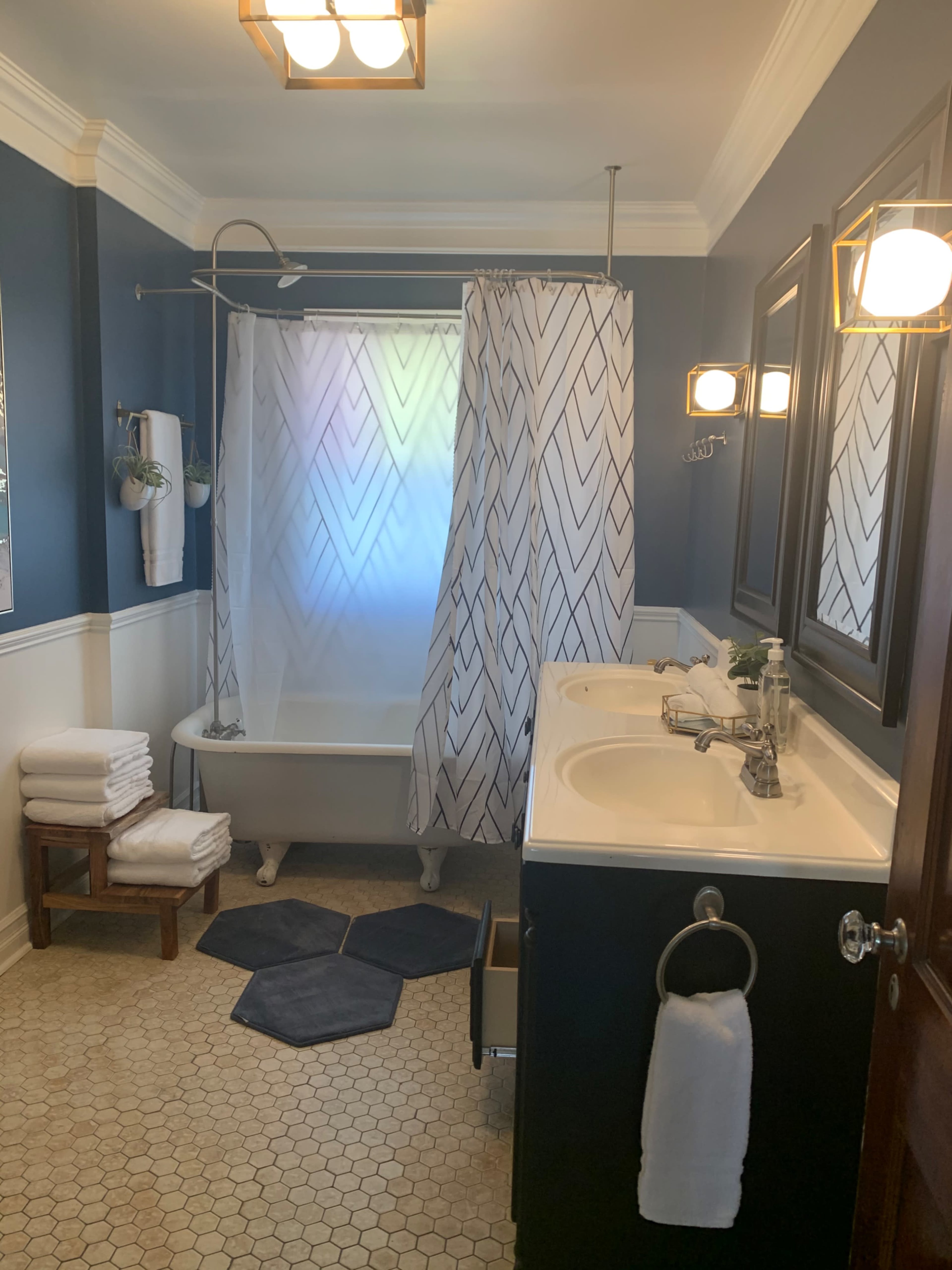 The image shows a bathroom with a clawfoot tub, a patterned shower curtain, a double sink, and a hexagonal tile floor.