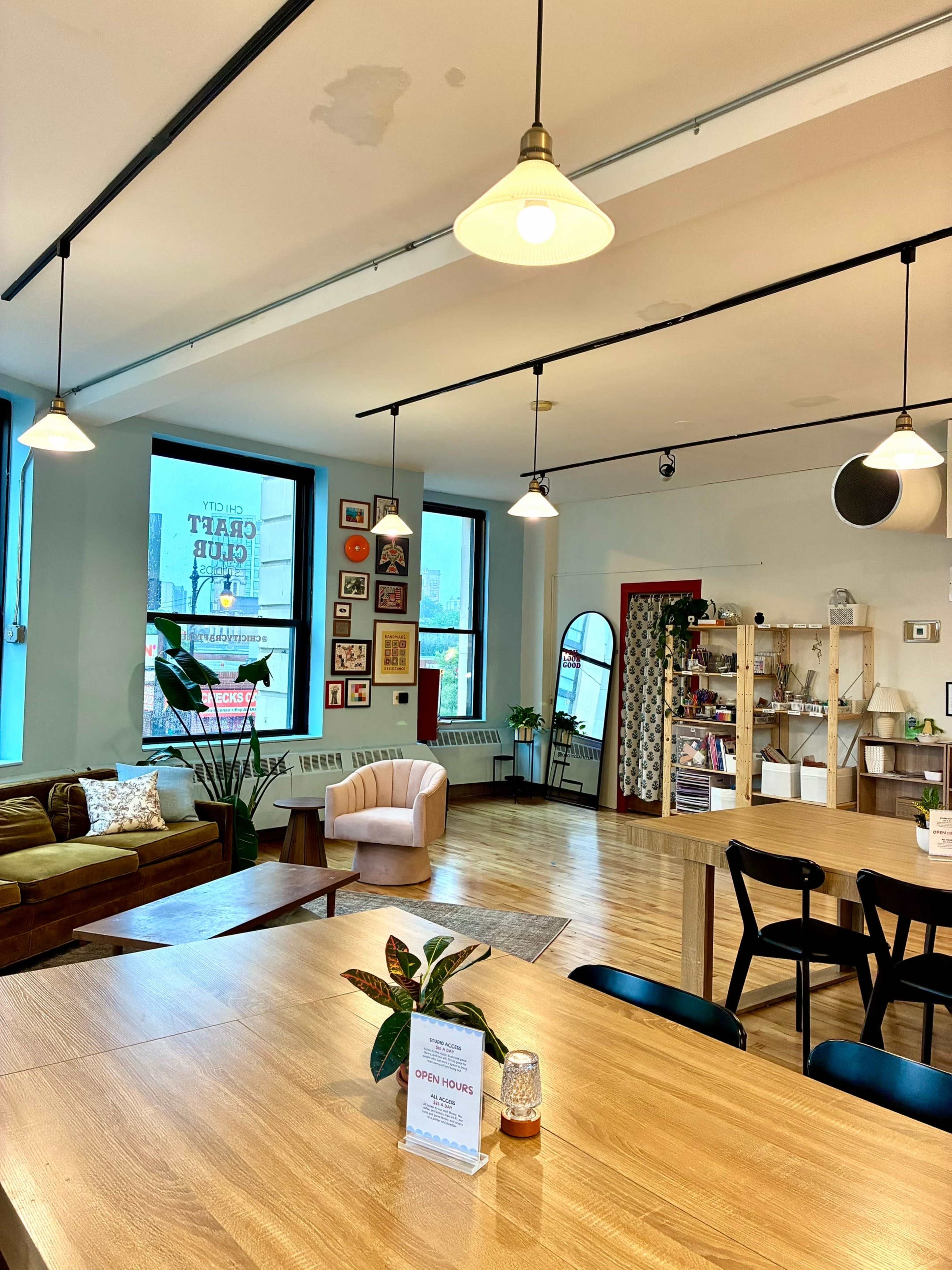 The image shows a cozy indoor common area featuring a wooden table with chairs, a green sofa, a light-colored armchair, and various decorations on the walls and shelves.