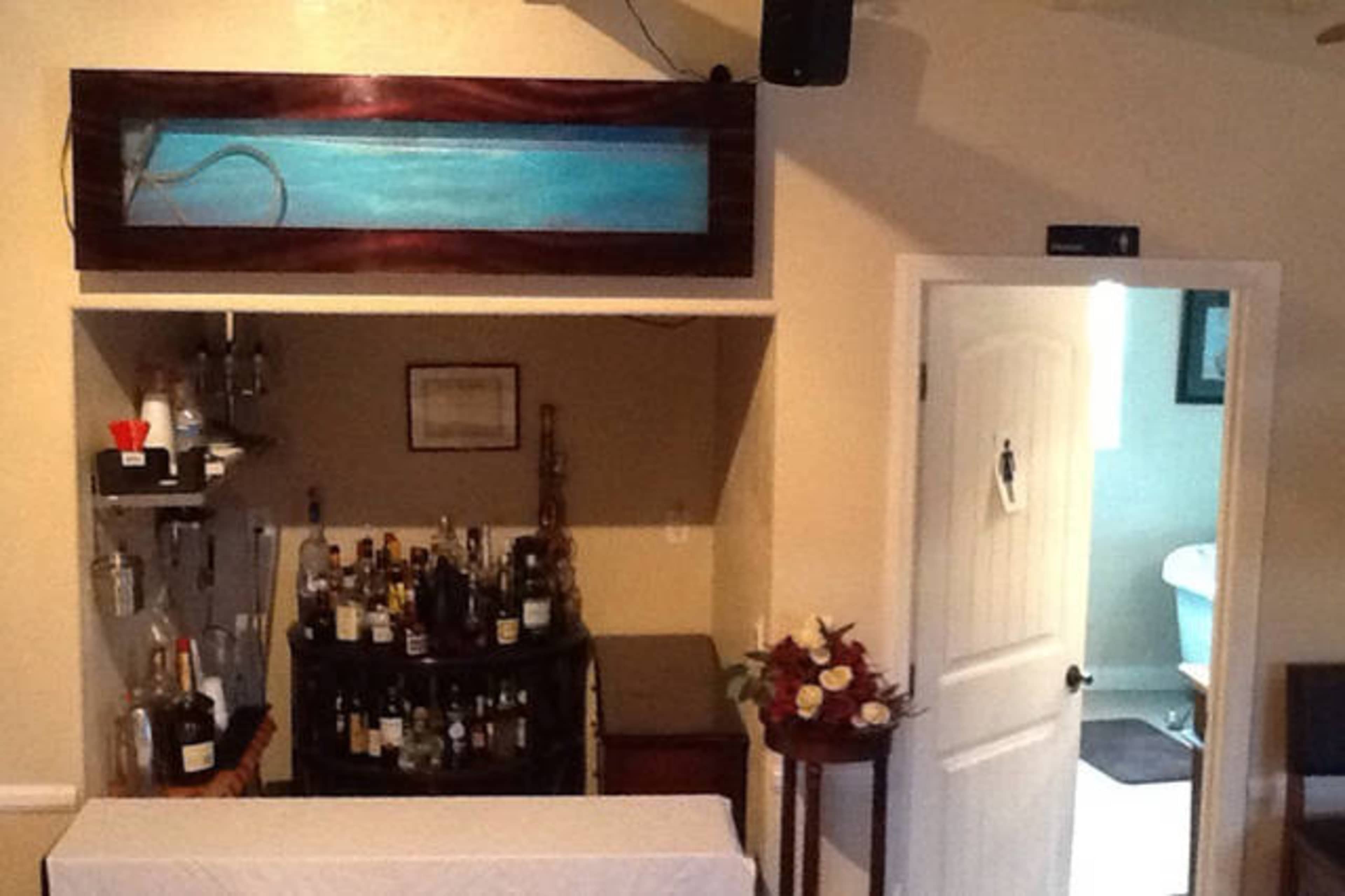 A small bar area with a variety of alcoholic beverages and a decorative aquarium above, alongside a door that leads to a restroom.