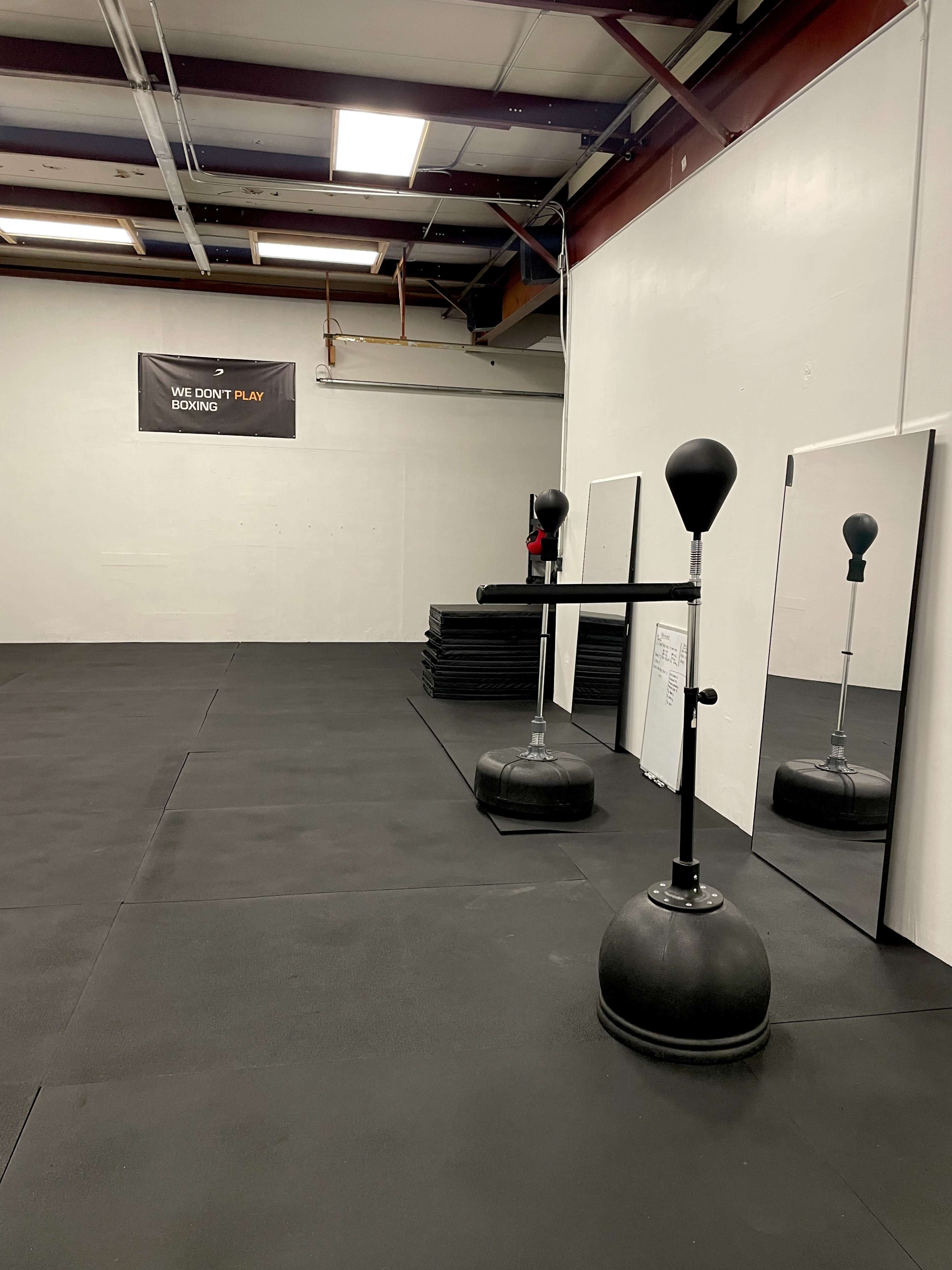 An empty gym space featuring a boxing bag, mirrors, and exercise mats on the floor.