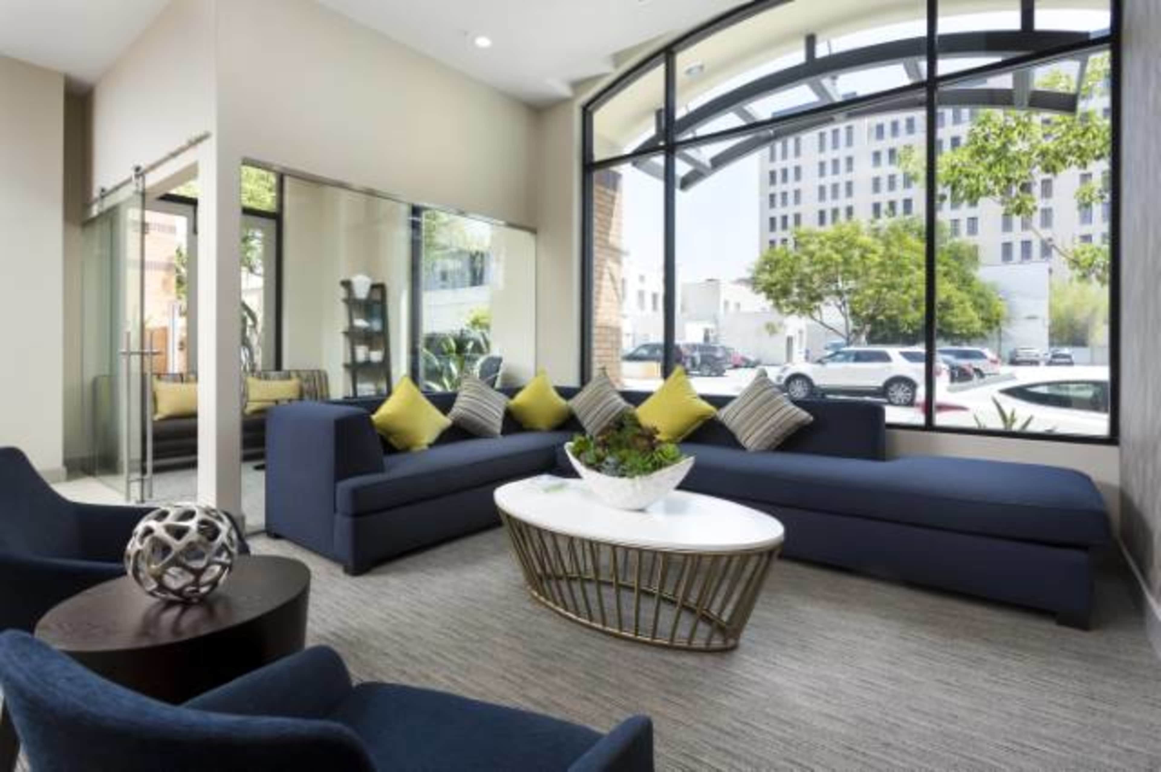 A modern lounge area features a navy sectional sofa, a round coffee table, and large windows overlooking a city street.