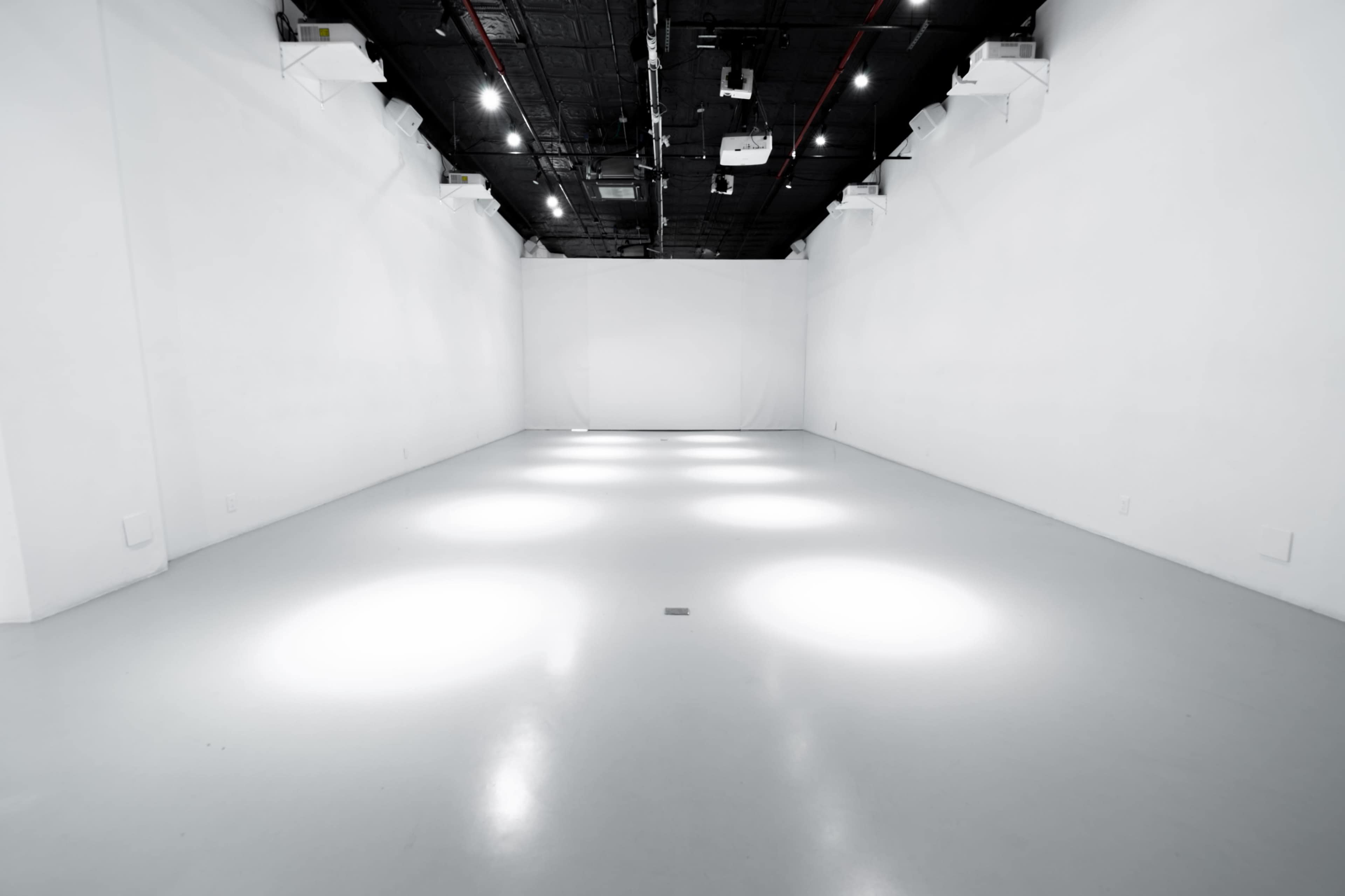 A spacious, empty room with white walls and a grey floor illuminated by several spotlights.
