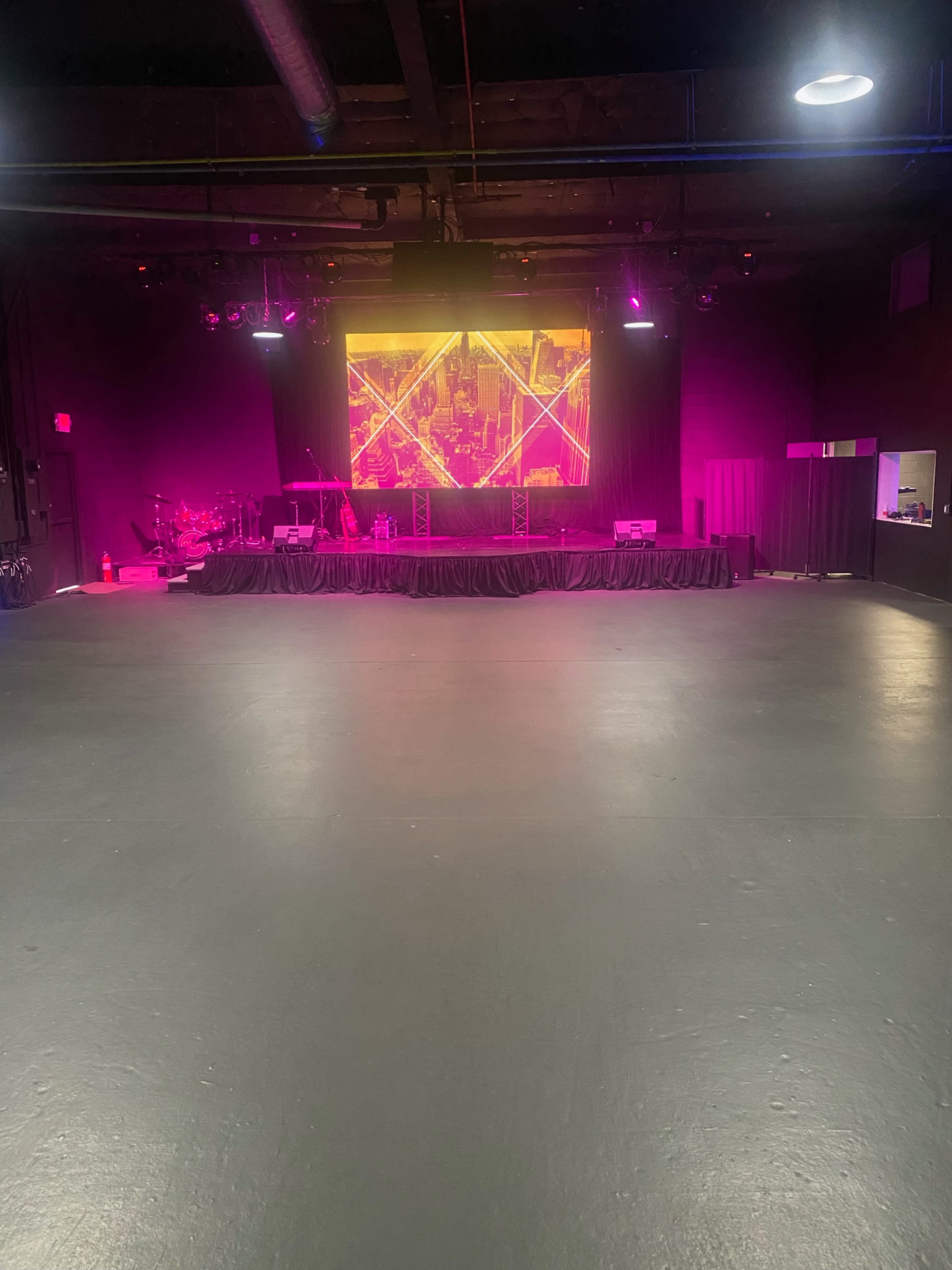 The image shows a spacious stage area with a large illuminated backdrop and musical instruments set up in the background.