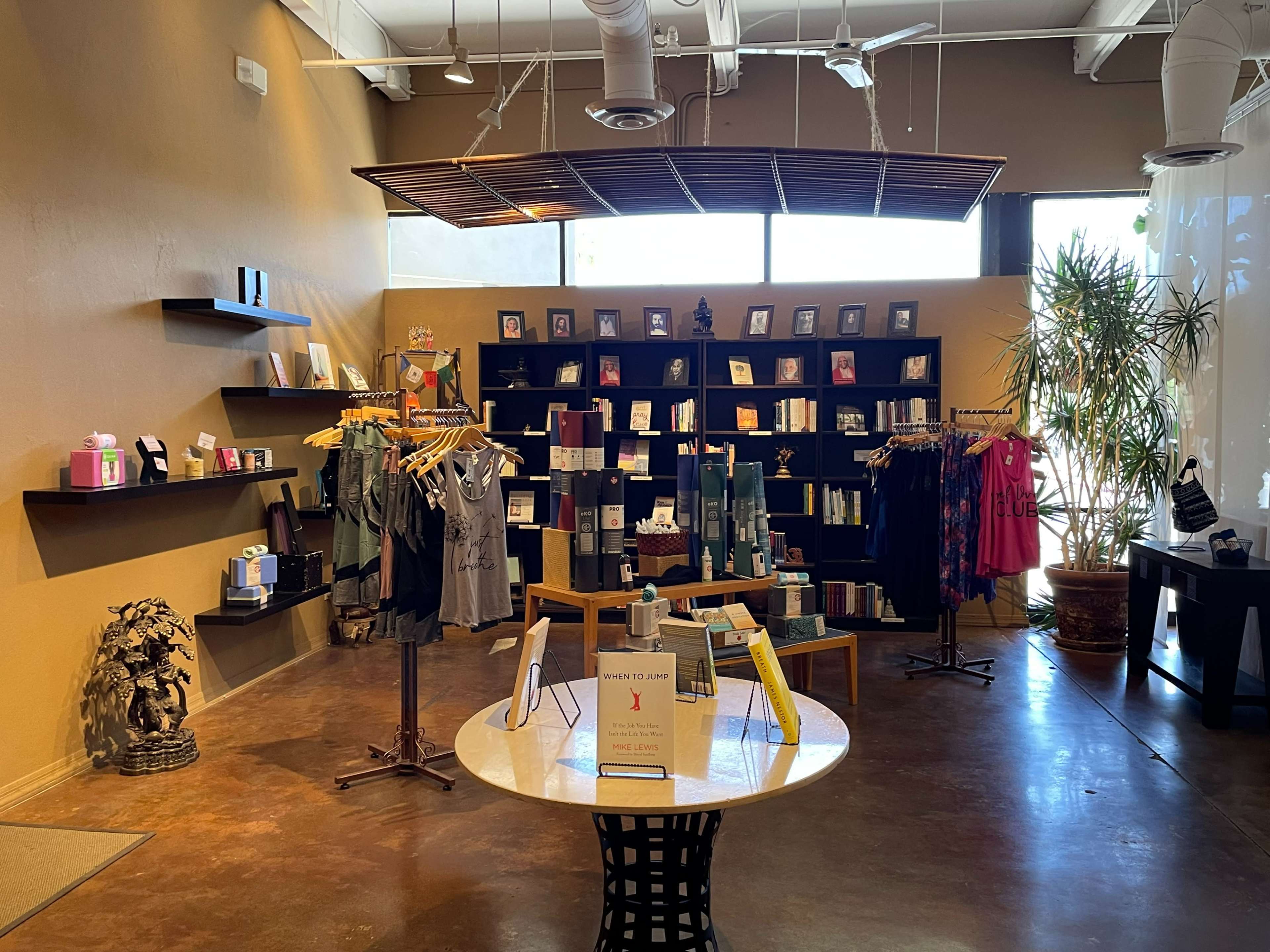 A retail space featuring shelves of products, clothing displays, and a central table in a sunlit room with large windows.