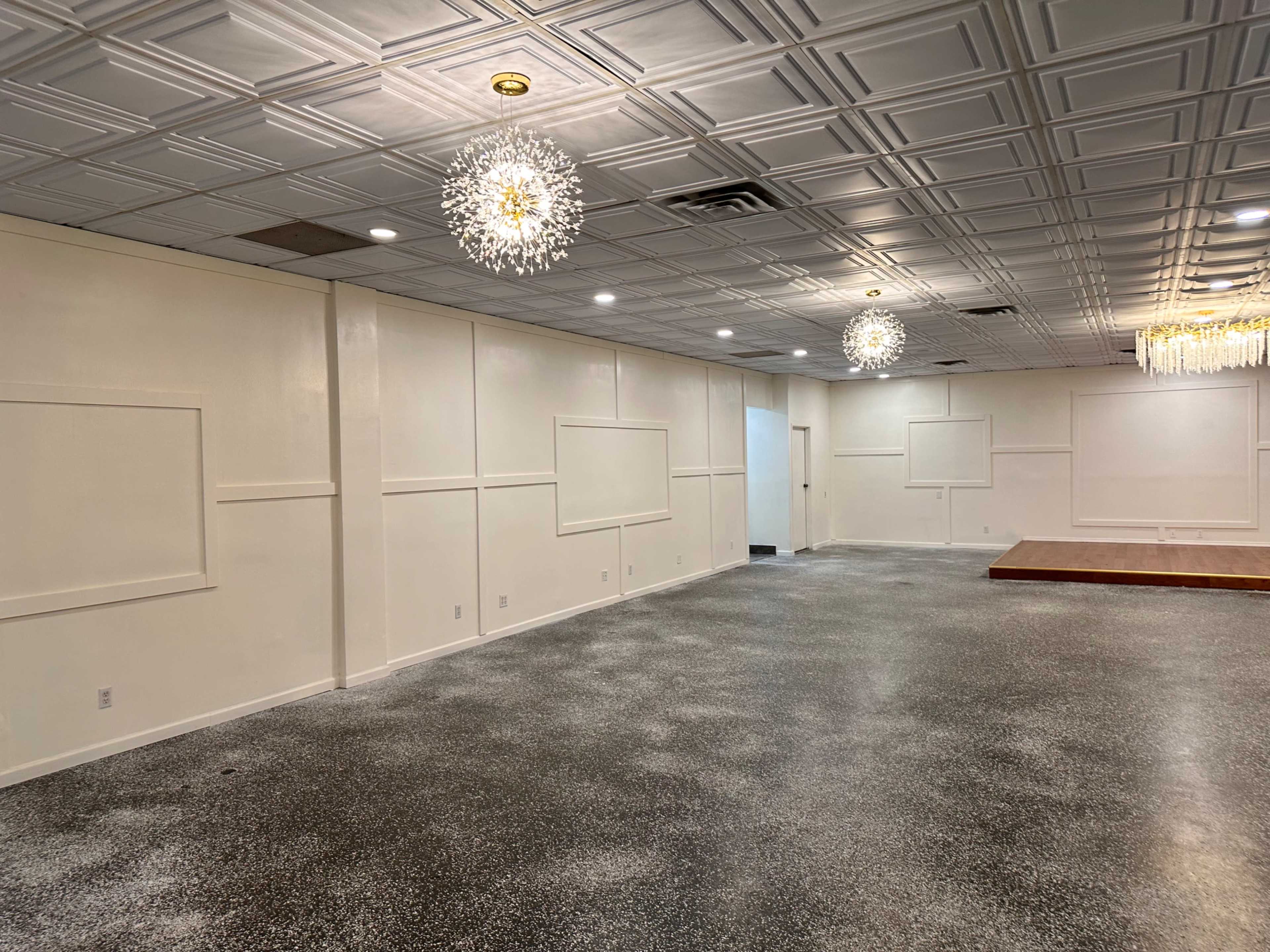 A spacious interior room with a polished floor, white walls featuring decorative panels, and several hanging light fixtures.