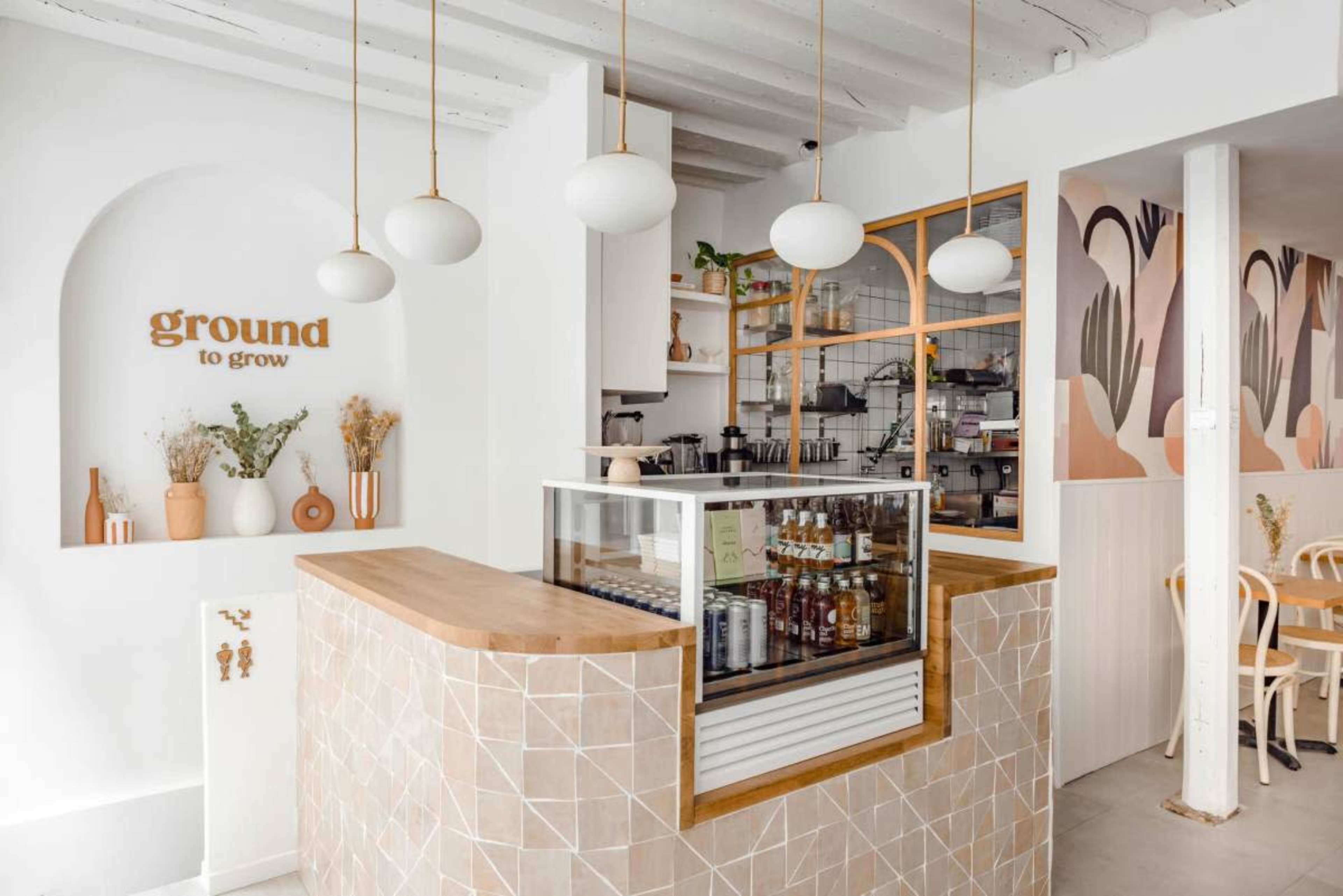 The image shows a modern café interior with a light color palette, featuring a wooden counter with a glass display case and decorative elements on the walls.