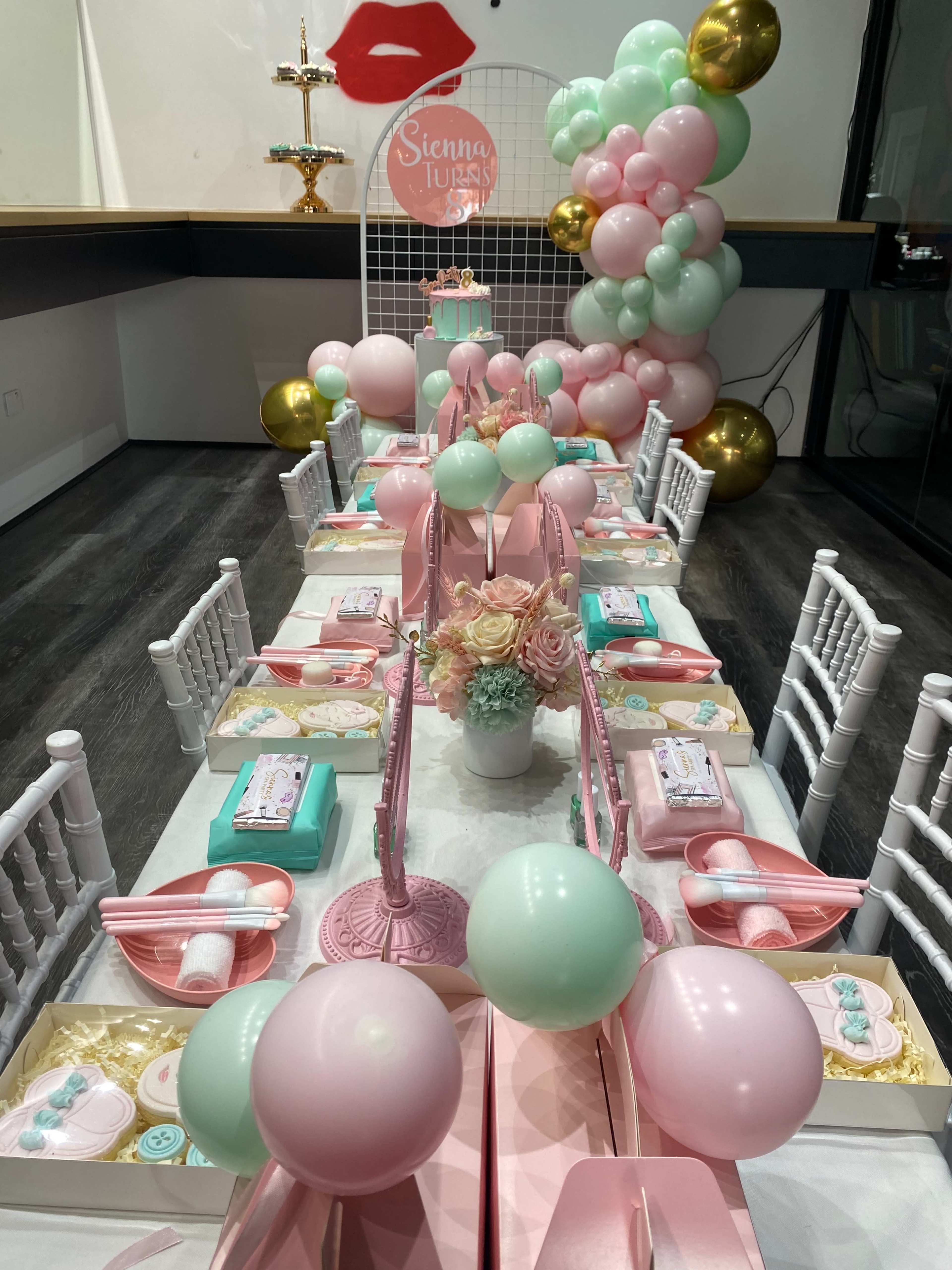 A festive table is set with pastel-colored decorations, party favors, and a backdrop featuring a lip-themed design.