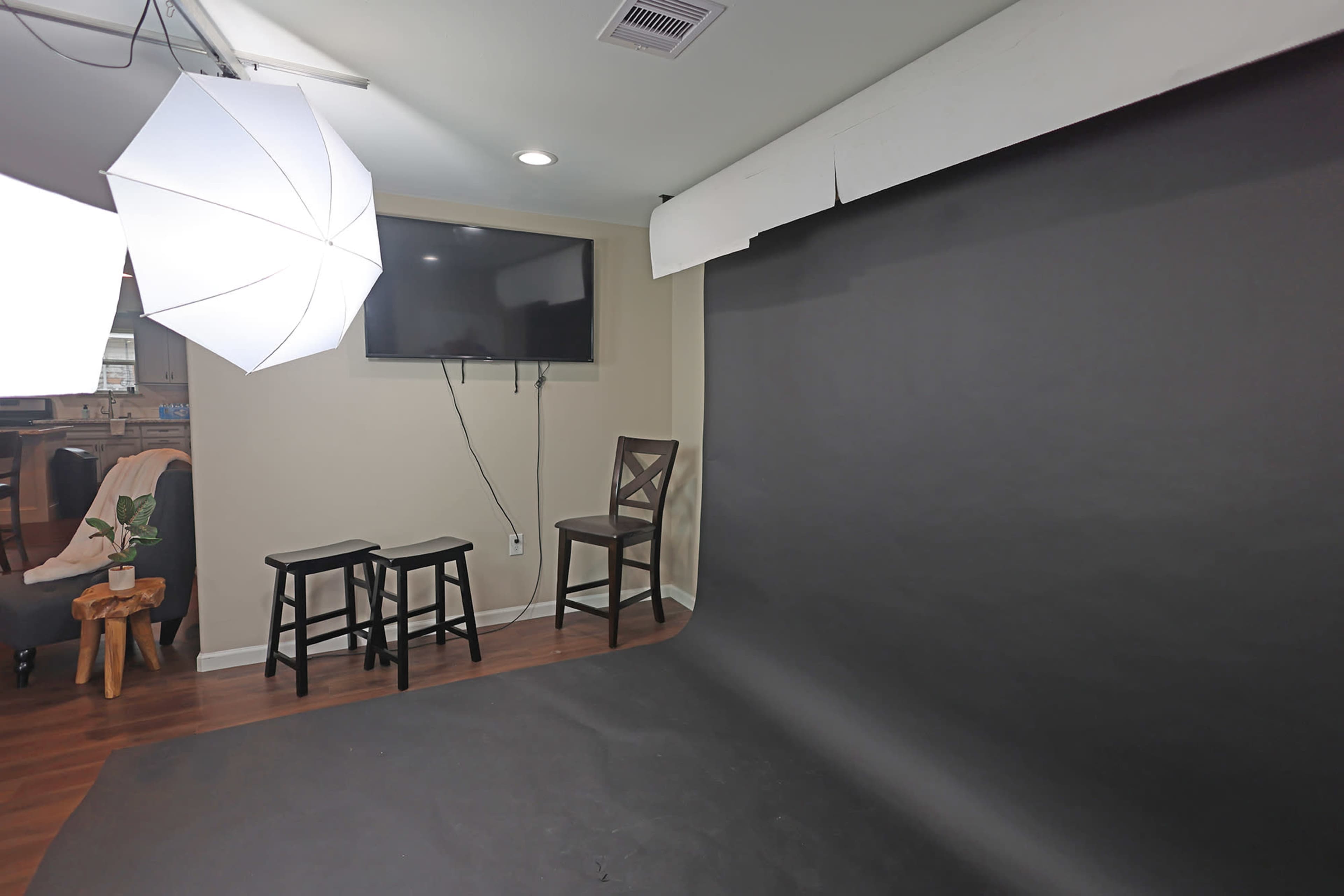 A simple indoor photography setup featuring a black backdrop, two stools, a television on the wall, and softbox lighting.