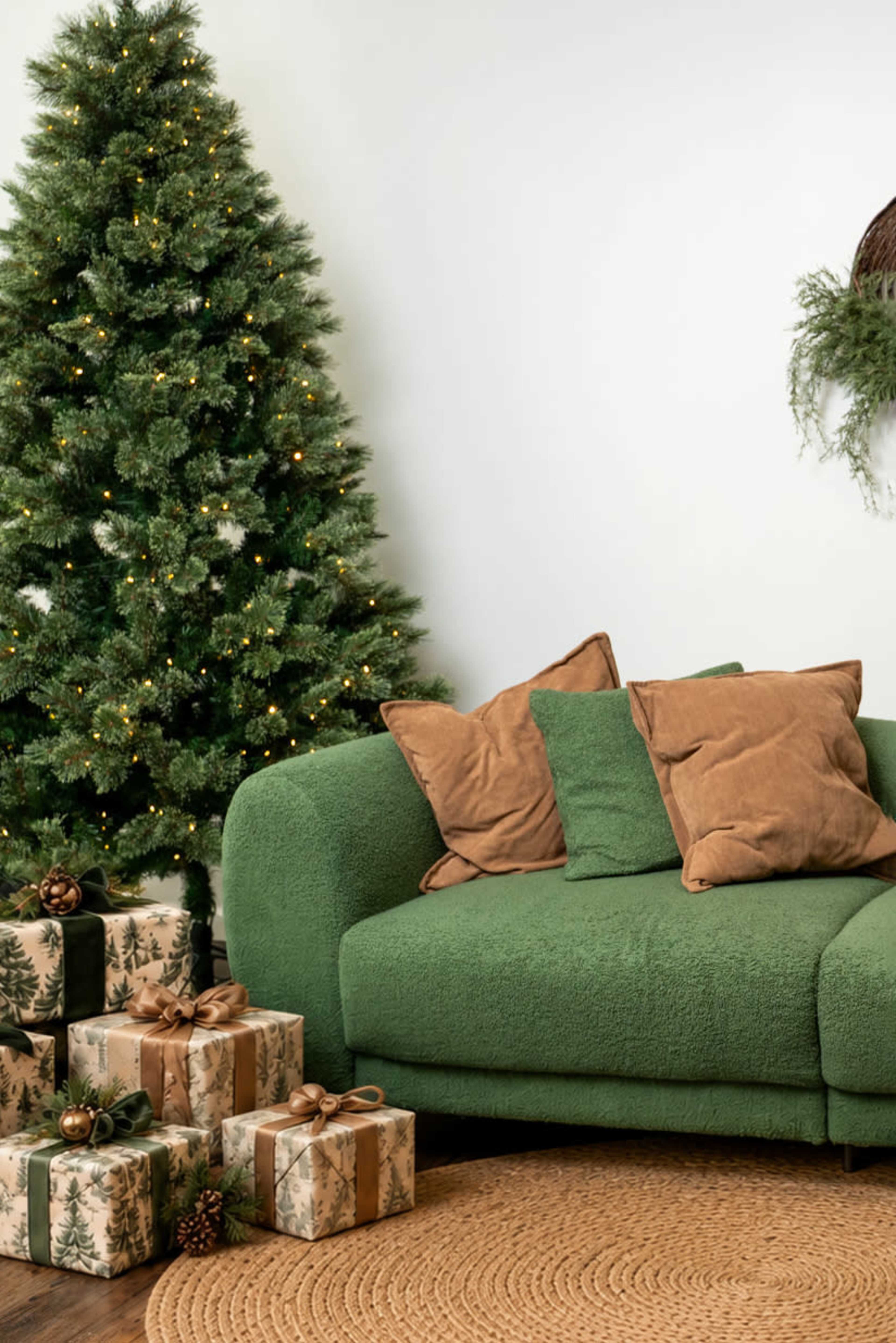 A cozy green sofa adorned with brown pillows sits near a decorated Christmas tree and wrapped gifts on the floor.