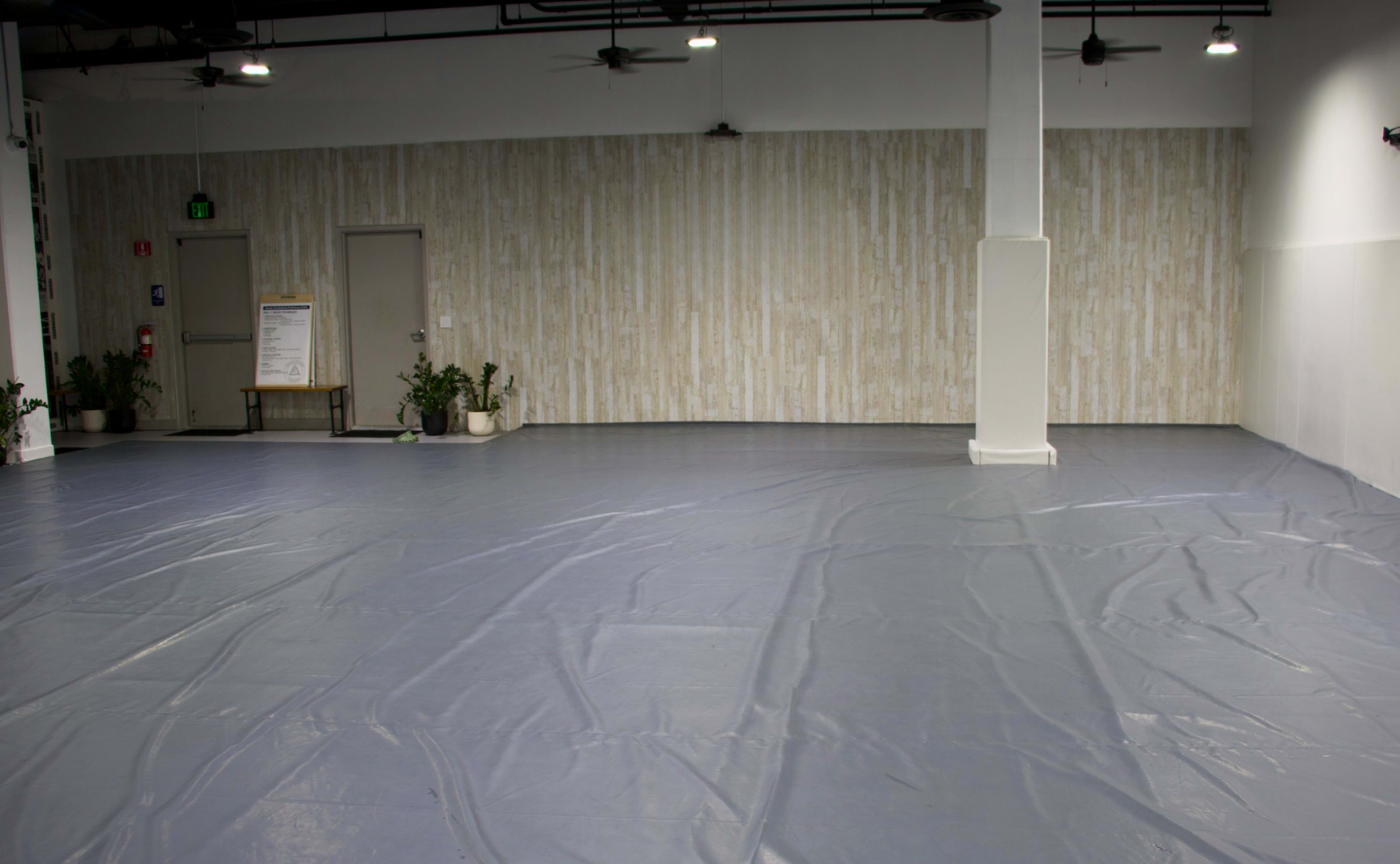 The image shows a large, empty indoor space with a smooth, blue tarp-like floor and a light-colored, textured wall in the background.