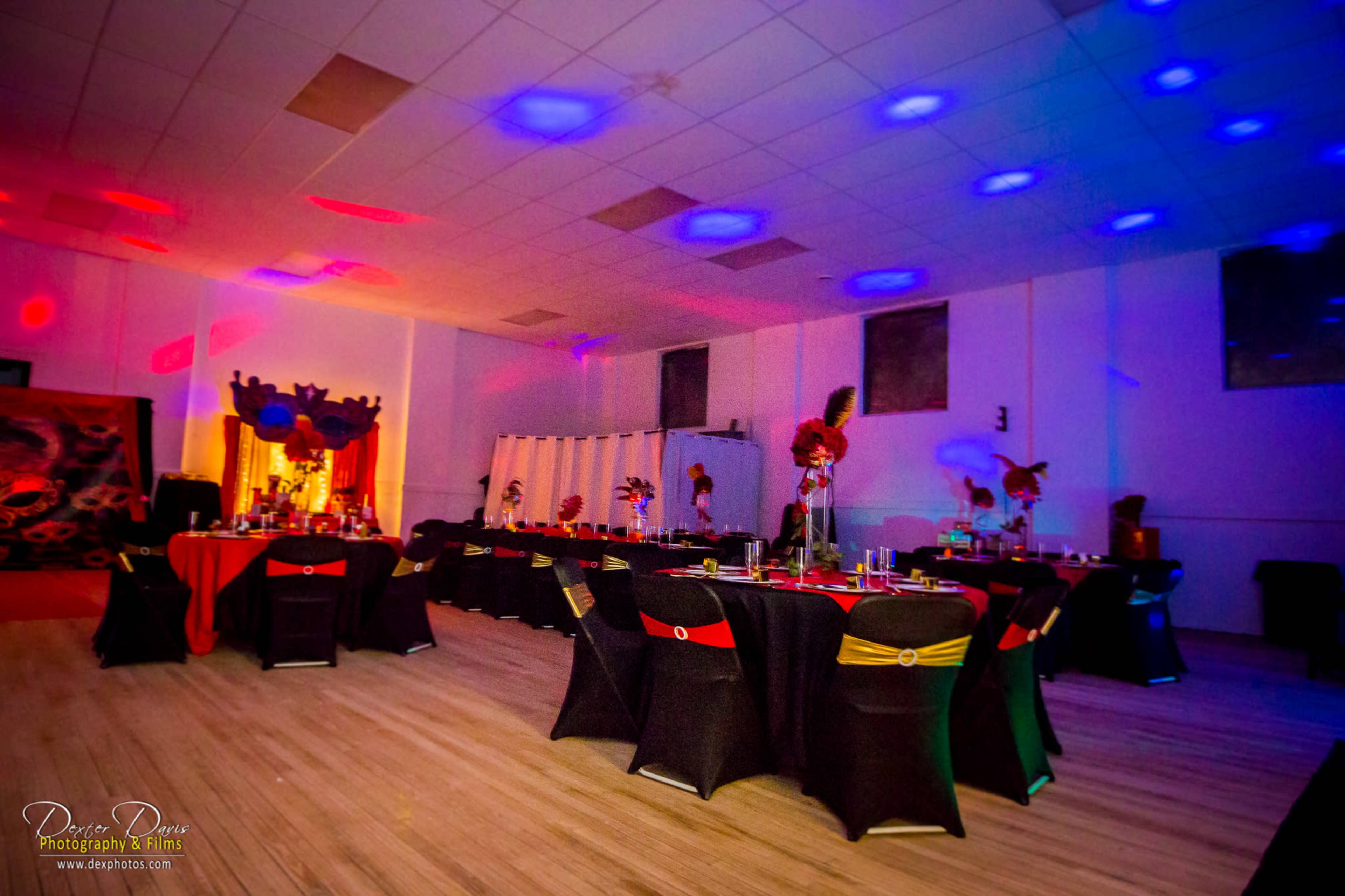 A large event space features tables set with dark tablecloths and colorful centerpieces, illuminated by colorful lights on the ceiling.