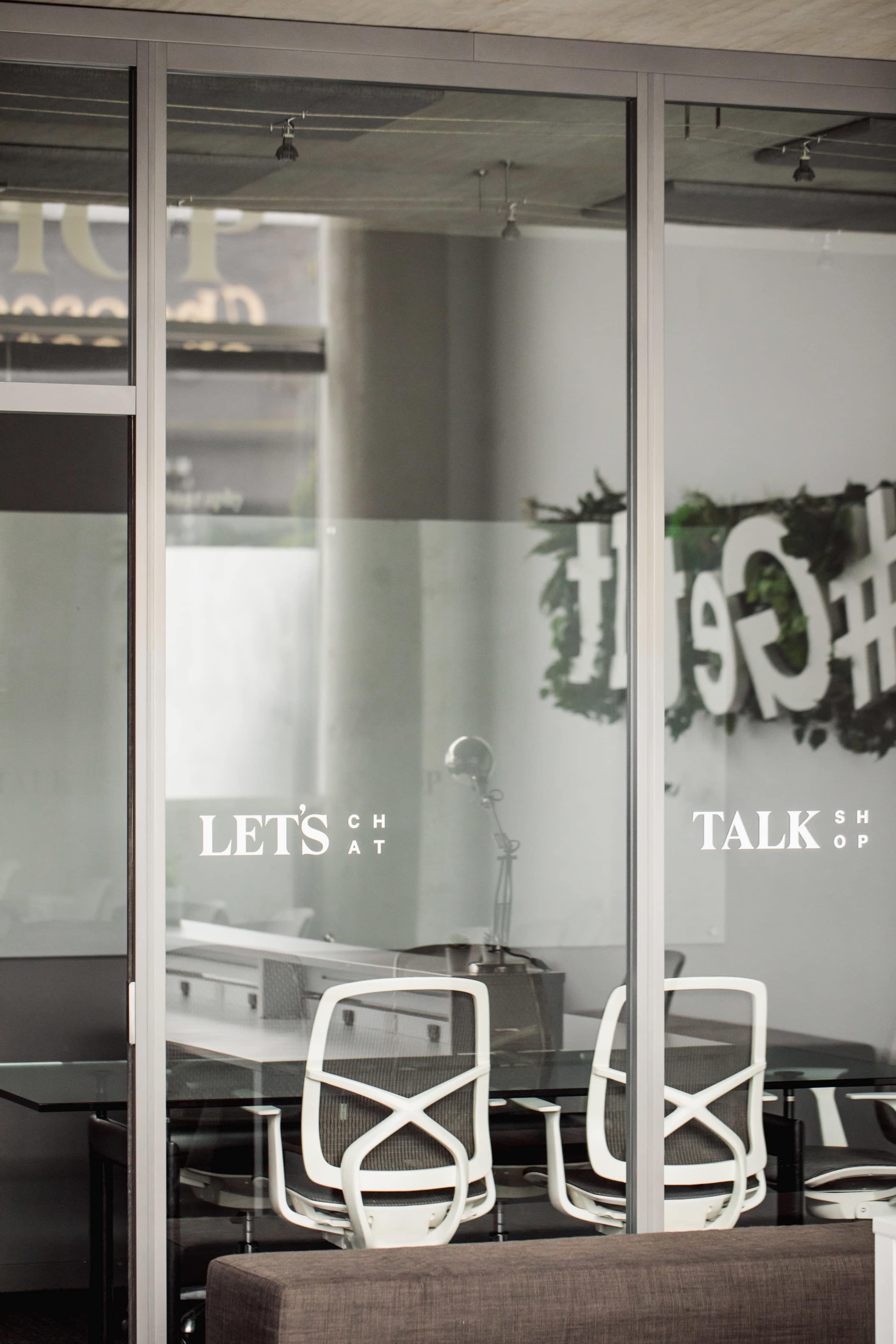 A modern office space with glass walls and a sign that reads "LET'S TALK SHOP" displayed on the door.