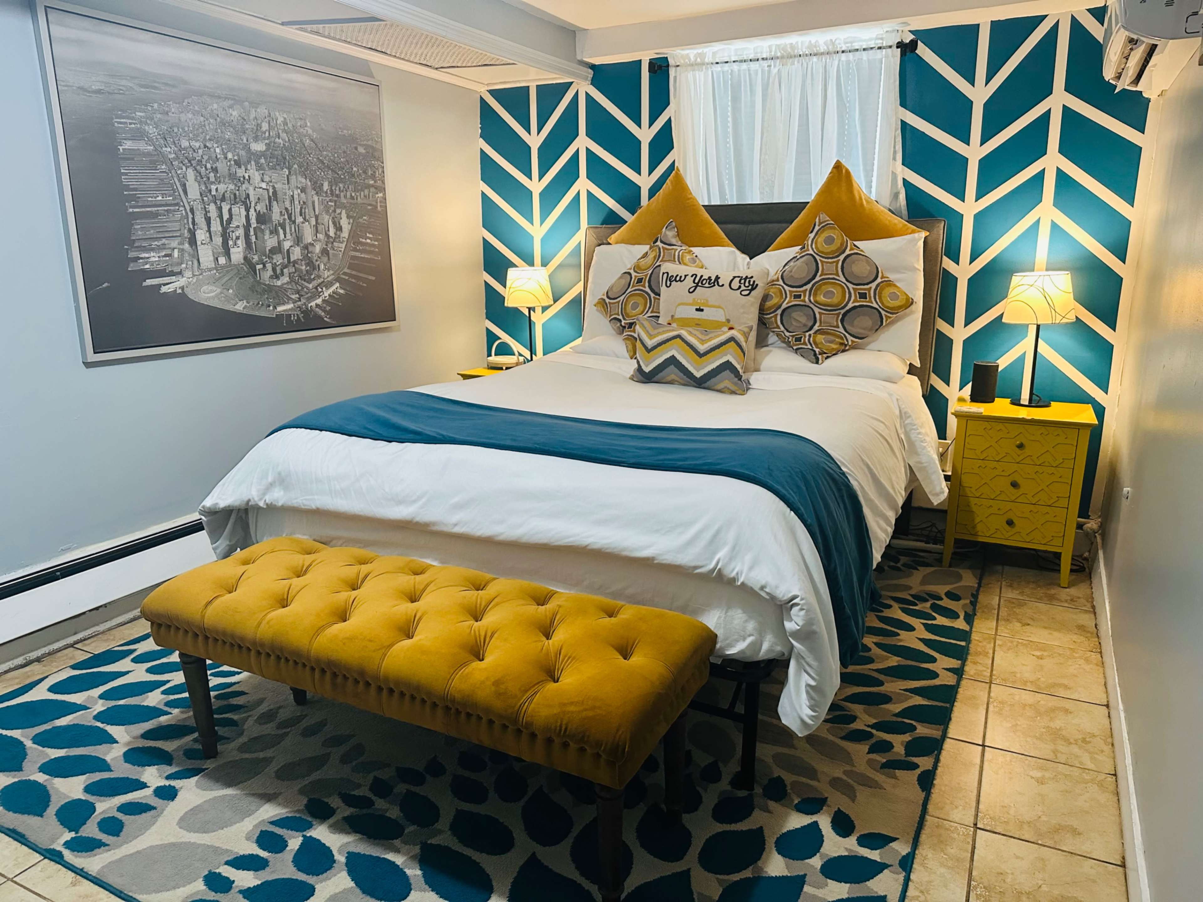 A cozy bedroom featuring a bed with decorative pillows, a yellow bench, and a geometric-patterned accent wall.