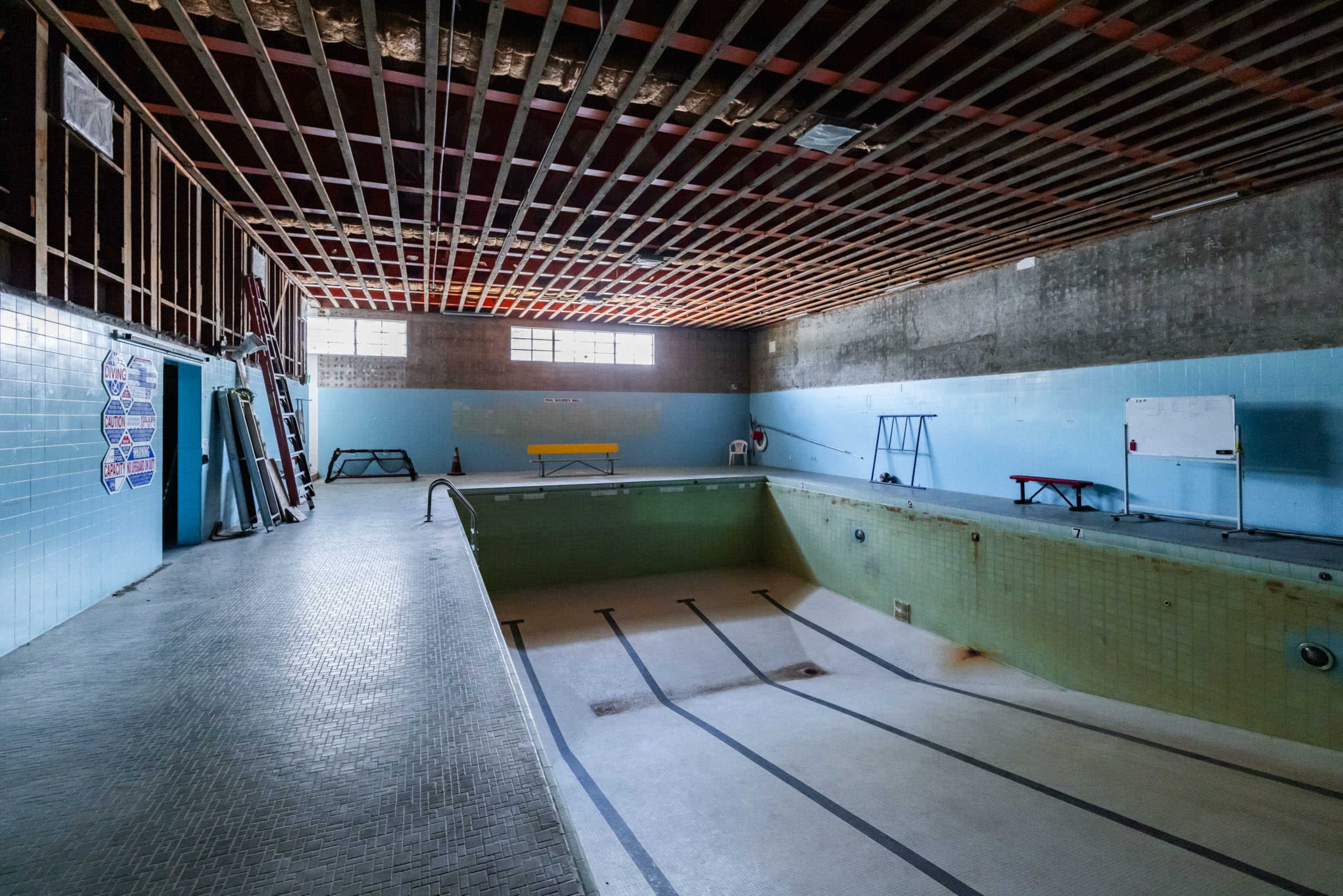 An empty indoor swimming pool with bare walls and exposed ceiling beams.