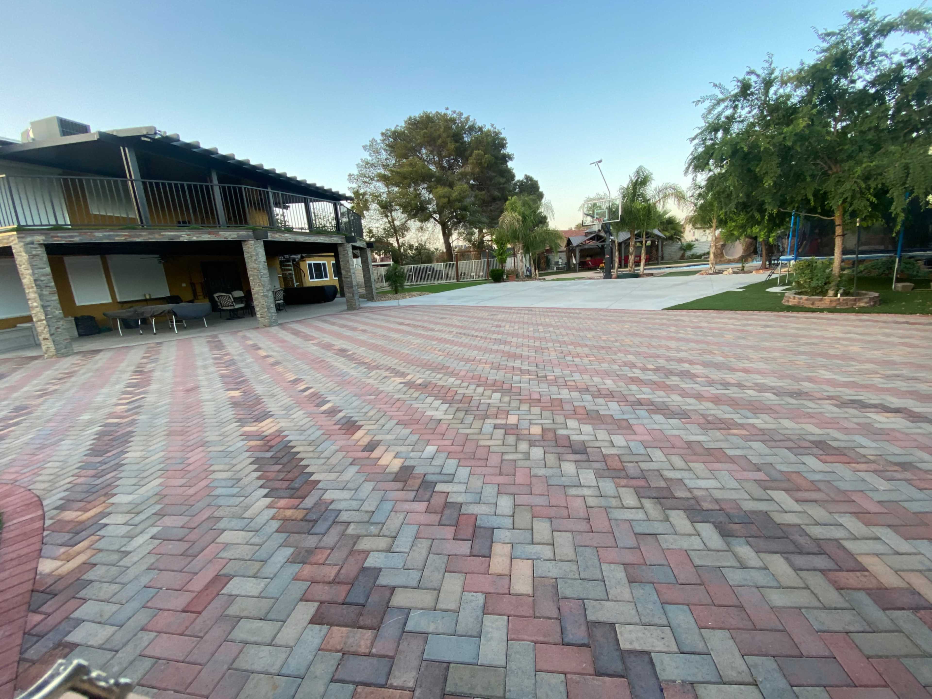 The image shows a spacious outdoor area with a paved surface, featuring a basketball court and a two-story building in the background.