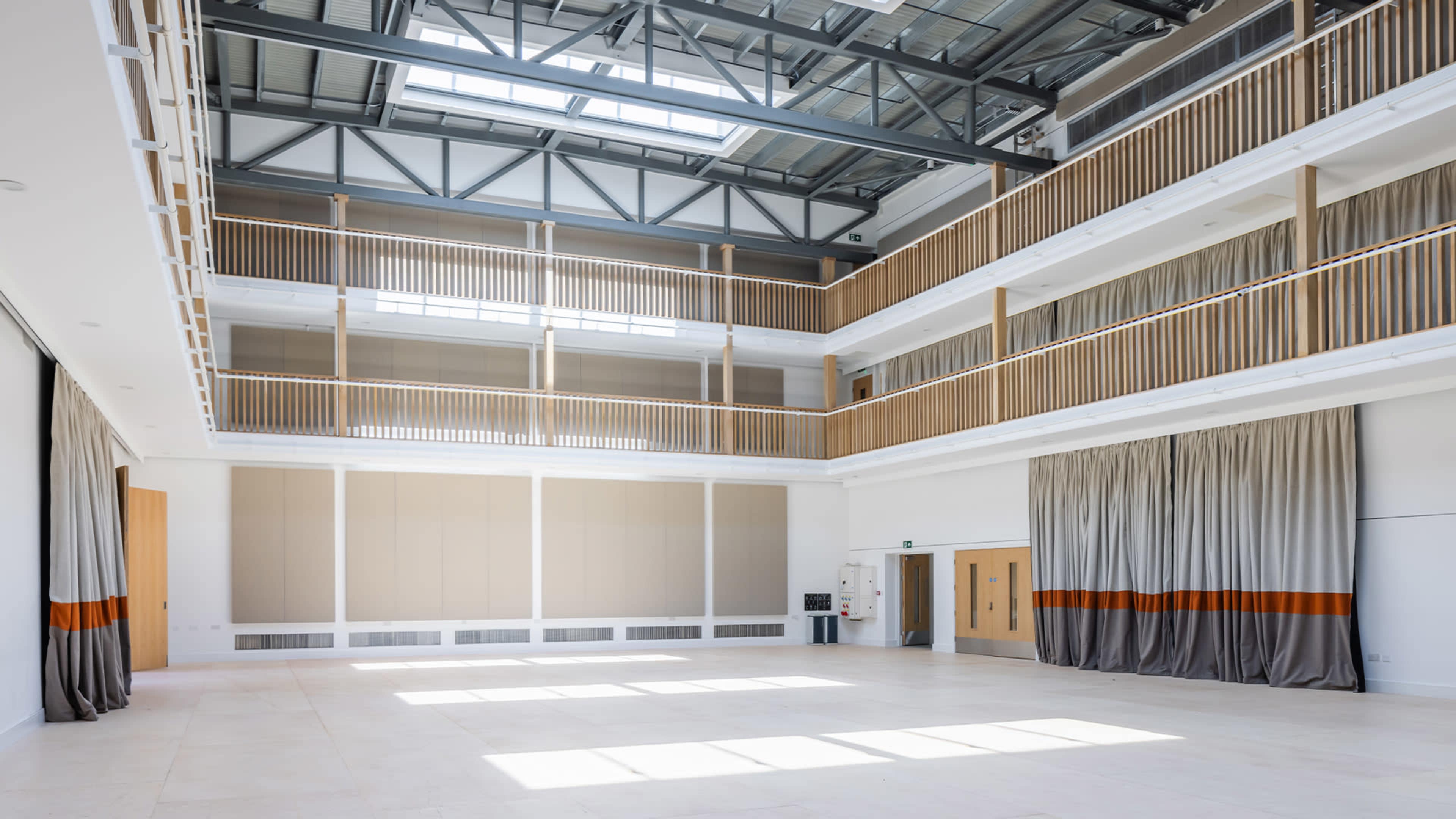 A spacious indoor area with multiple levels, featuring large windows and wooden railings, providing ample natural light.