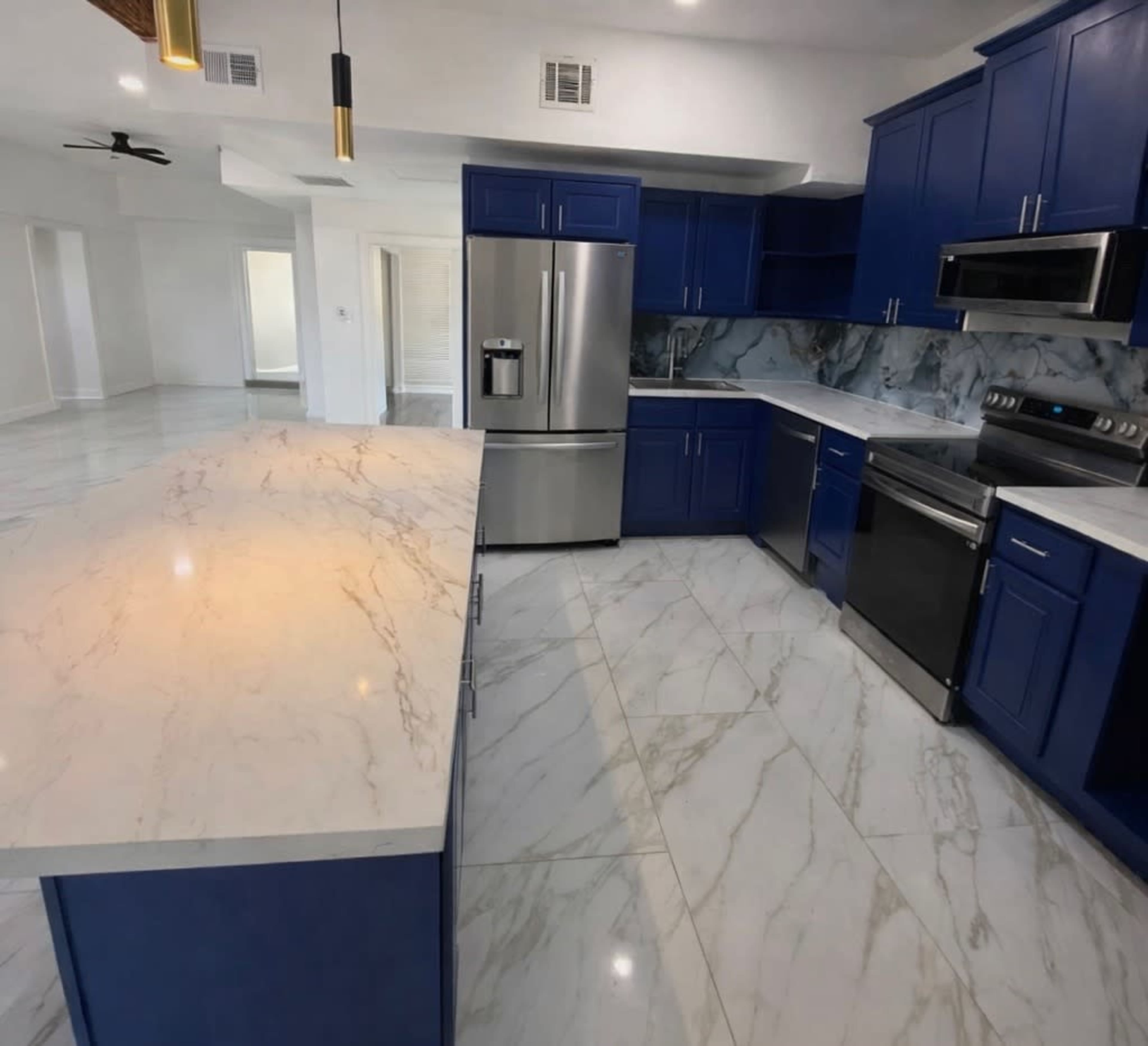 The image shows a modern kitchen featuring blue cabinets, stainless steel appliances, and a large marble countertop.