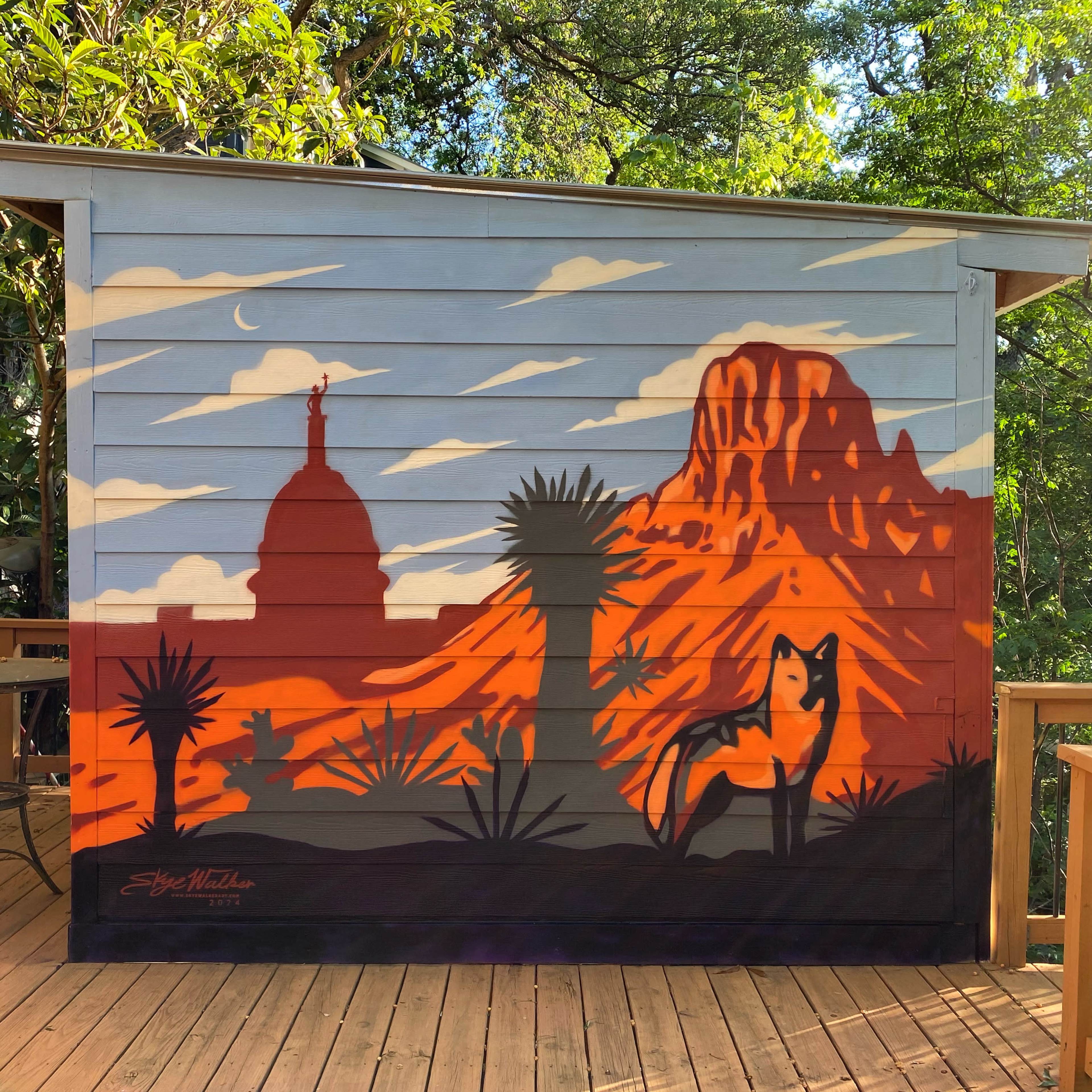 A vibrant mural depicting a desert landscape with a mountain, cacti, and a silhouette of a fox against a colorful twilight sky.