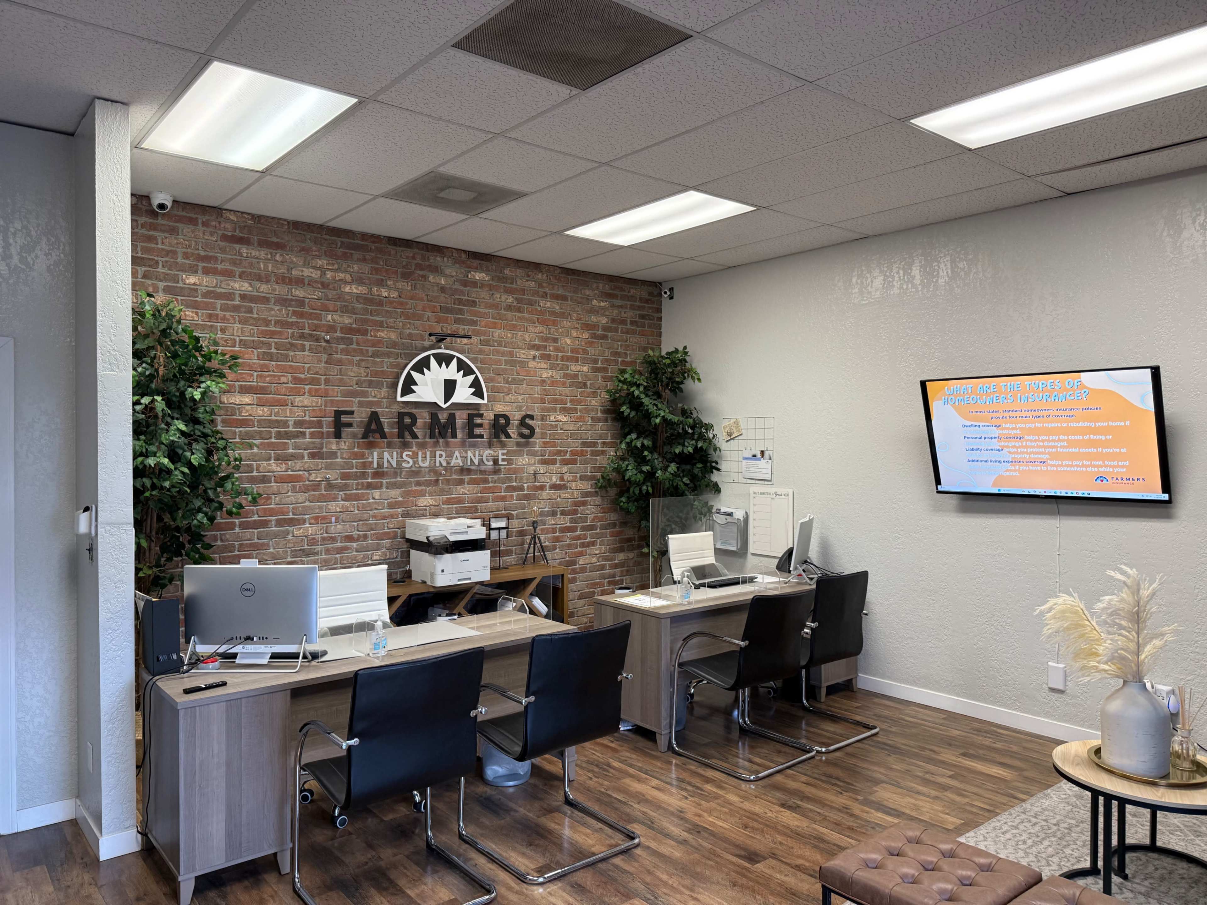 The image shows an office interior for Farmers Insurance, featuring desks, chairs, a television screen, and brick wall decor.