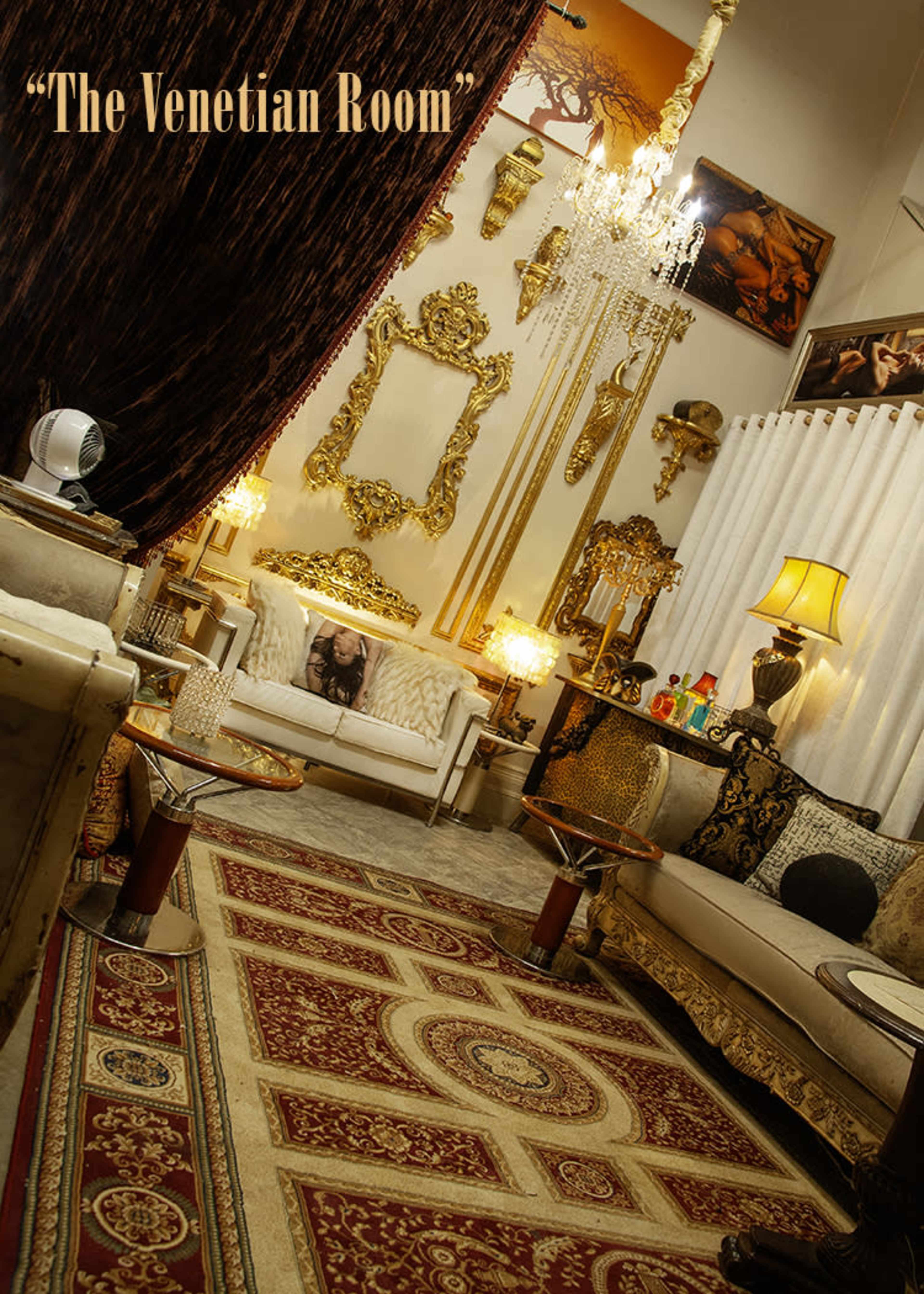 The image shows an elegantly decorated room featuring ornate furnishings, including a chandelier, patterned rugs, and elaborate wall decor.