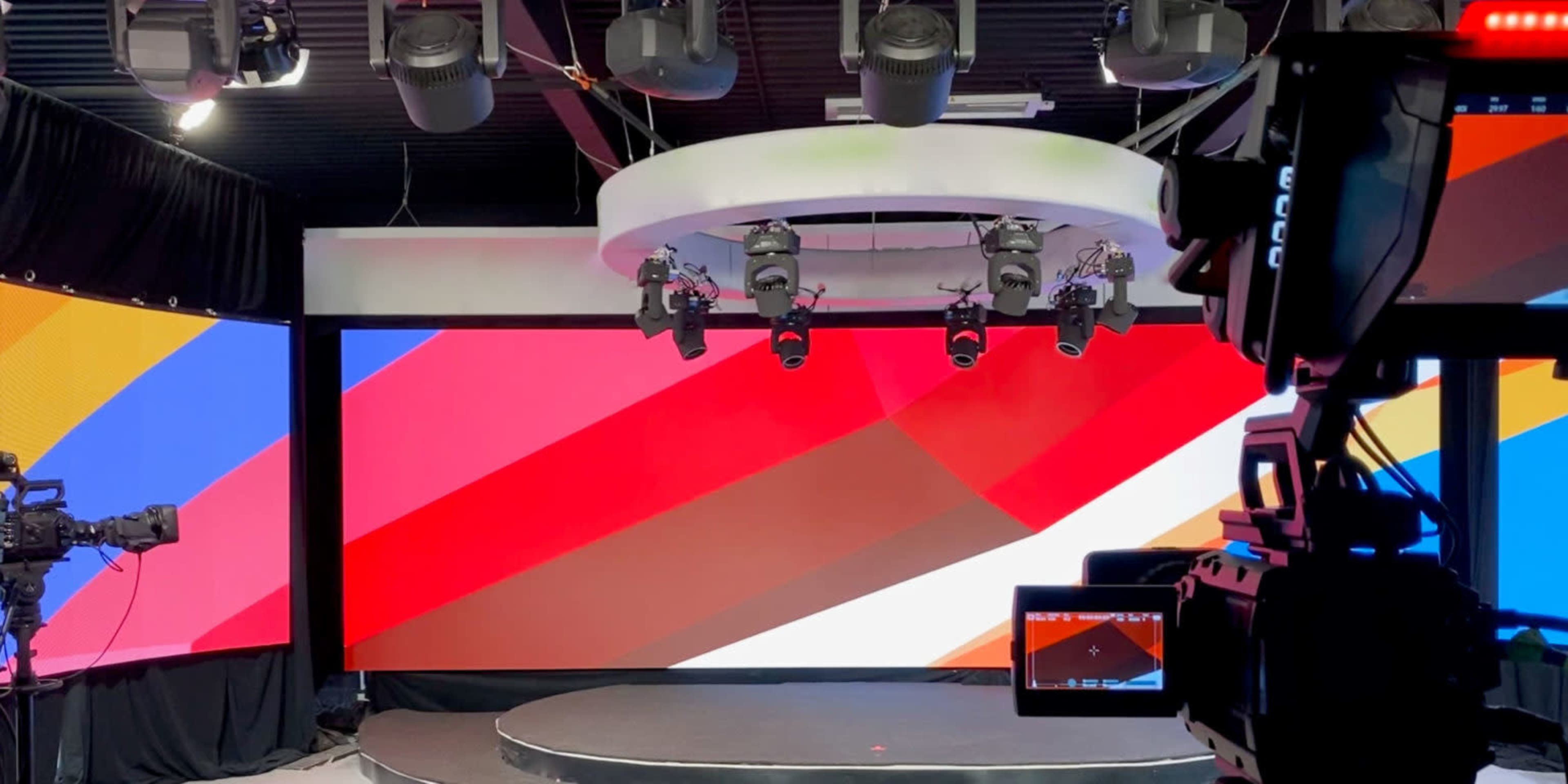 A television studio with a circular stage, colorful backdrop screens, and multiple studio lights.