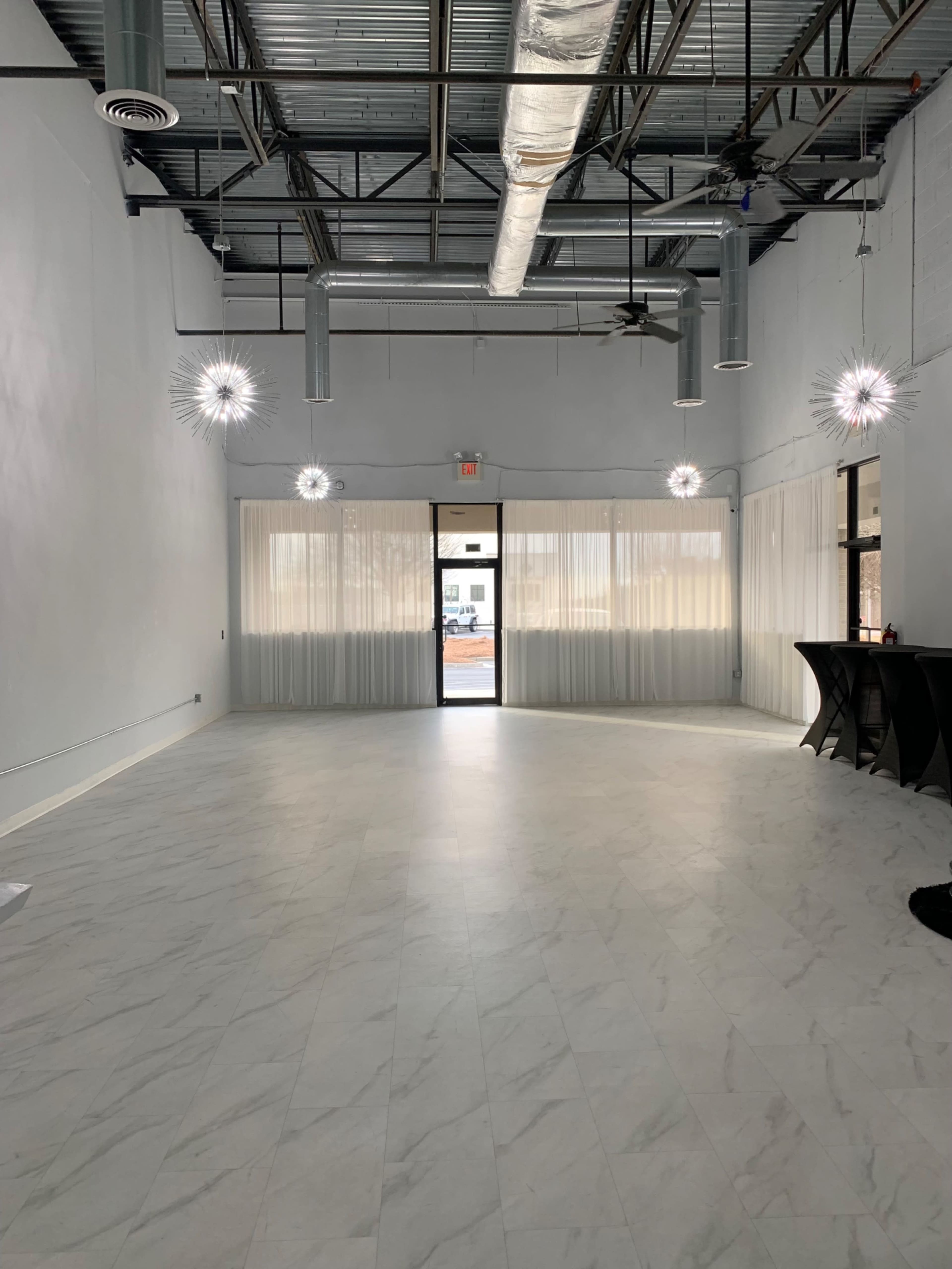 An empty, well-lit interior space with a marble-like floor, large windows, and decorative light fixtures hanging from the ceiling.