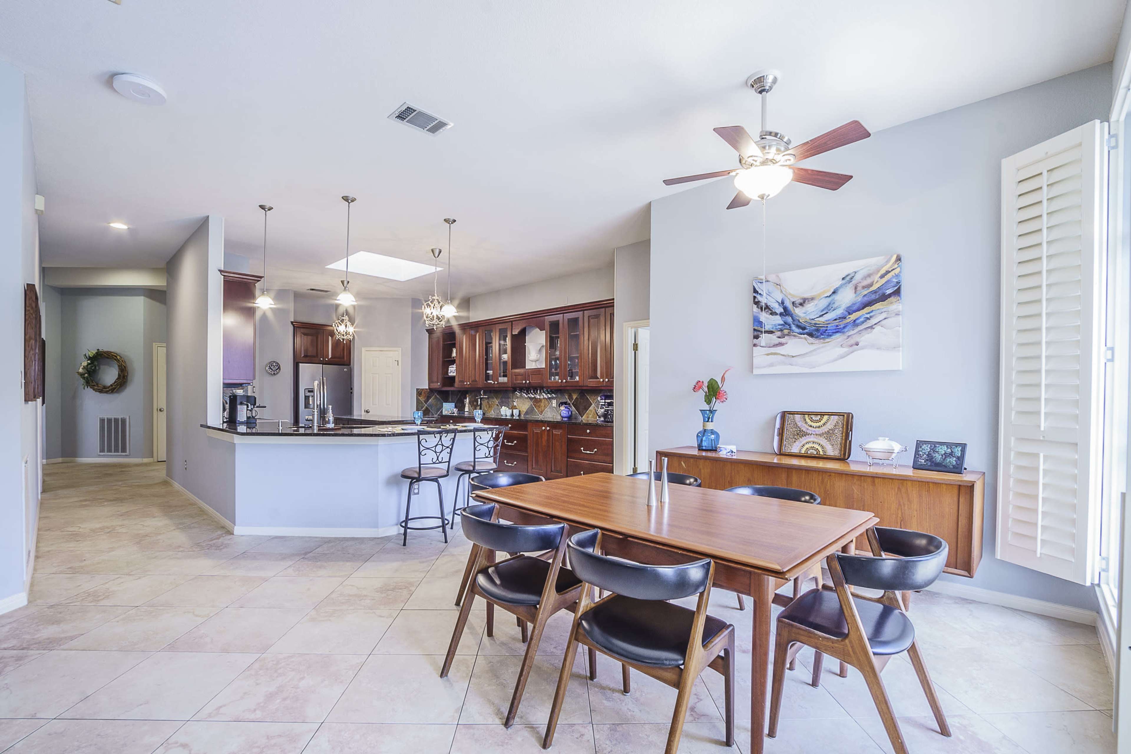 A modern kitchen and dining area features a large table surrounded by black chairs, with wooden cabinetry and a breakfast bar visible in the background.