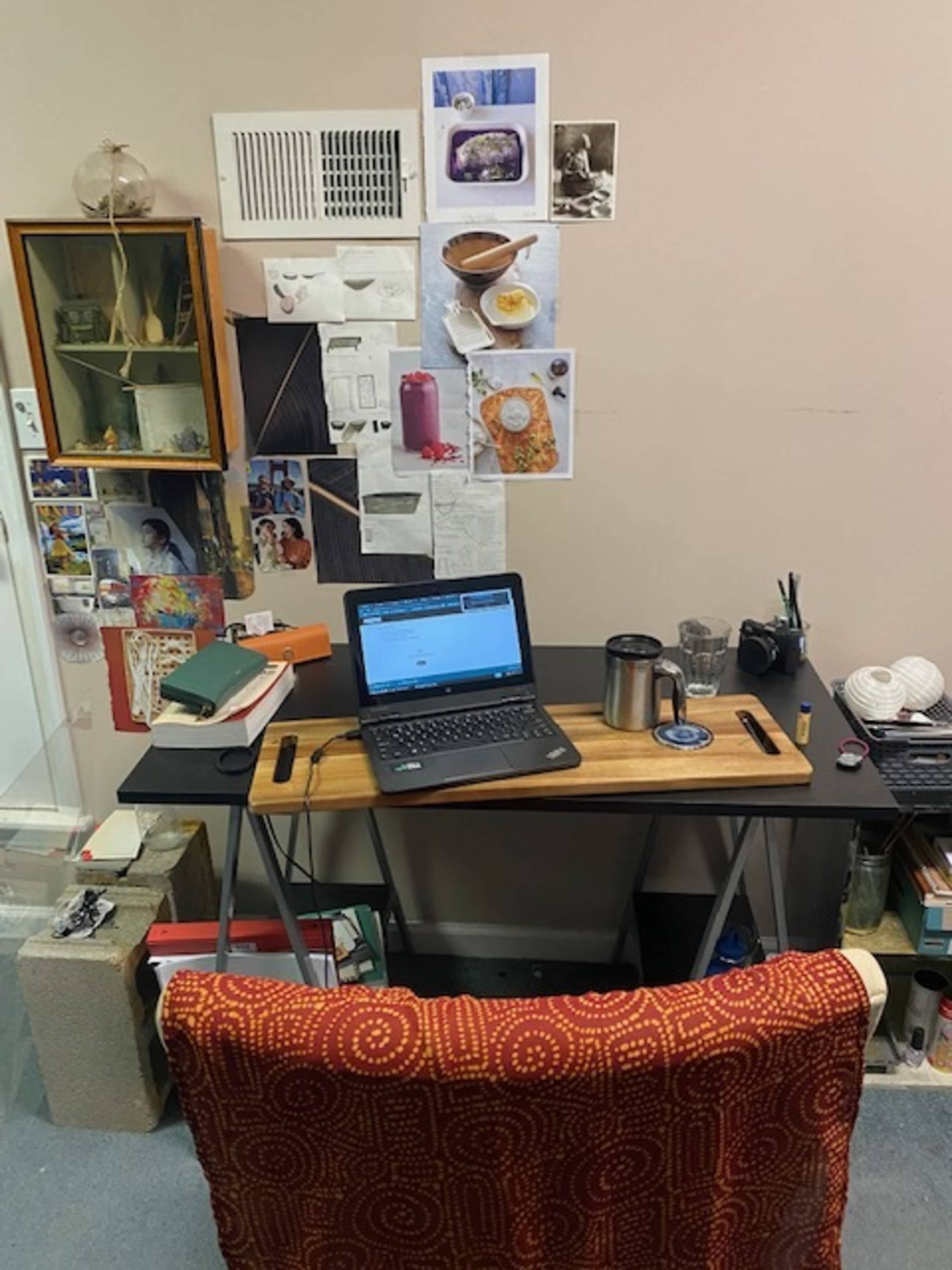 A desk with a laptop, notebooks, and various stationary items is positioned against a wall adorned with art and photographs.