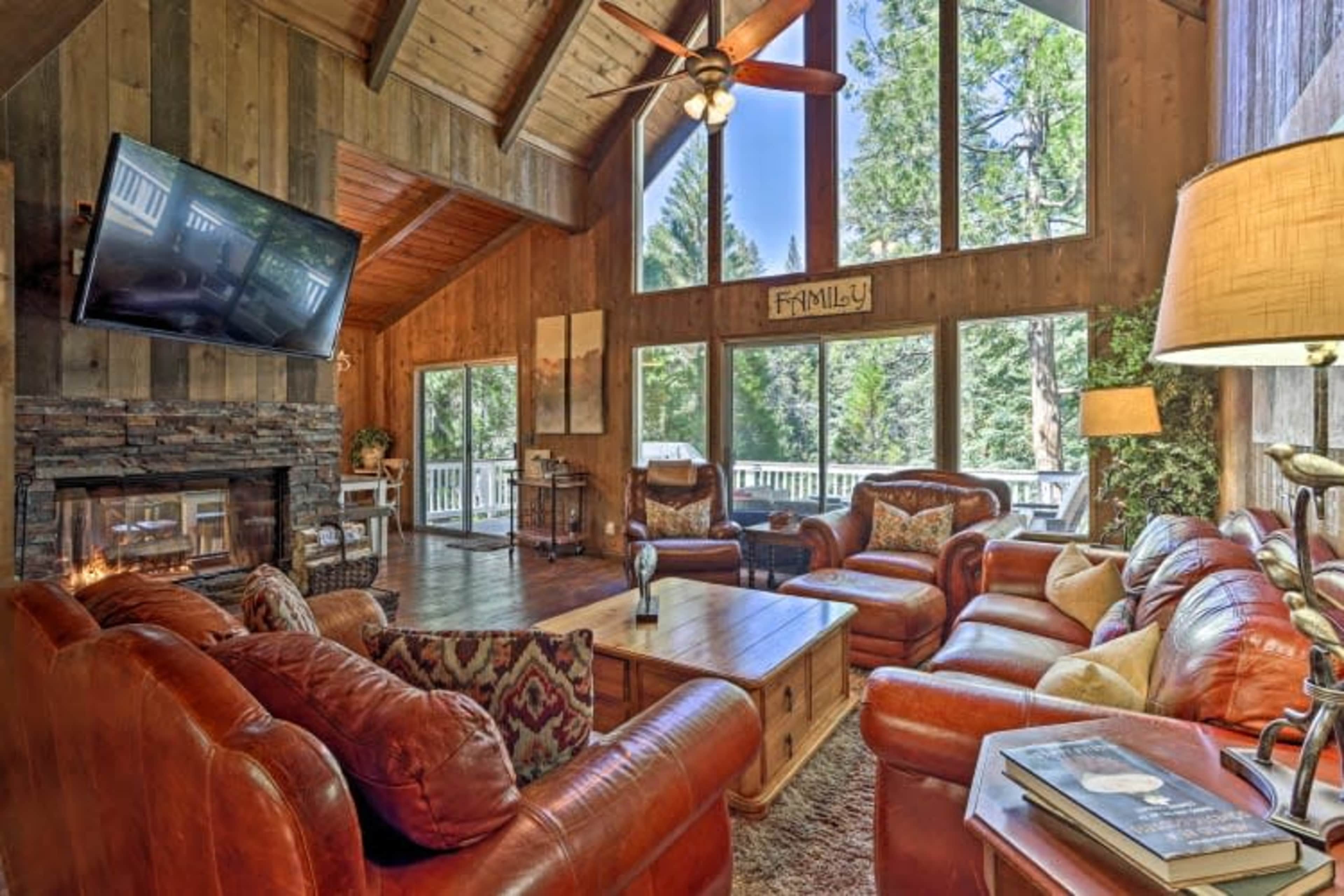 The interior of a cabin features a spacious seating area with leather sofas, a wooden coffee table, and large windows overlooking a forested landscape.