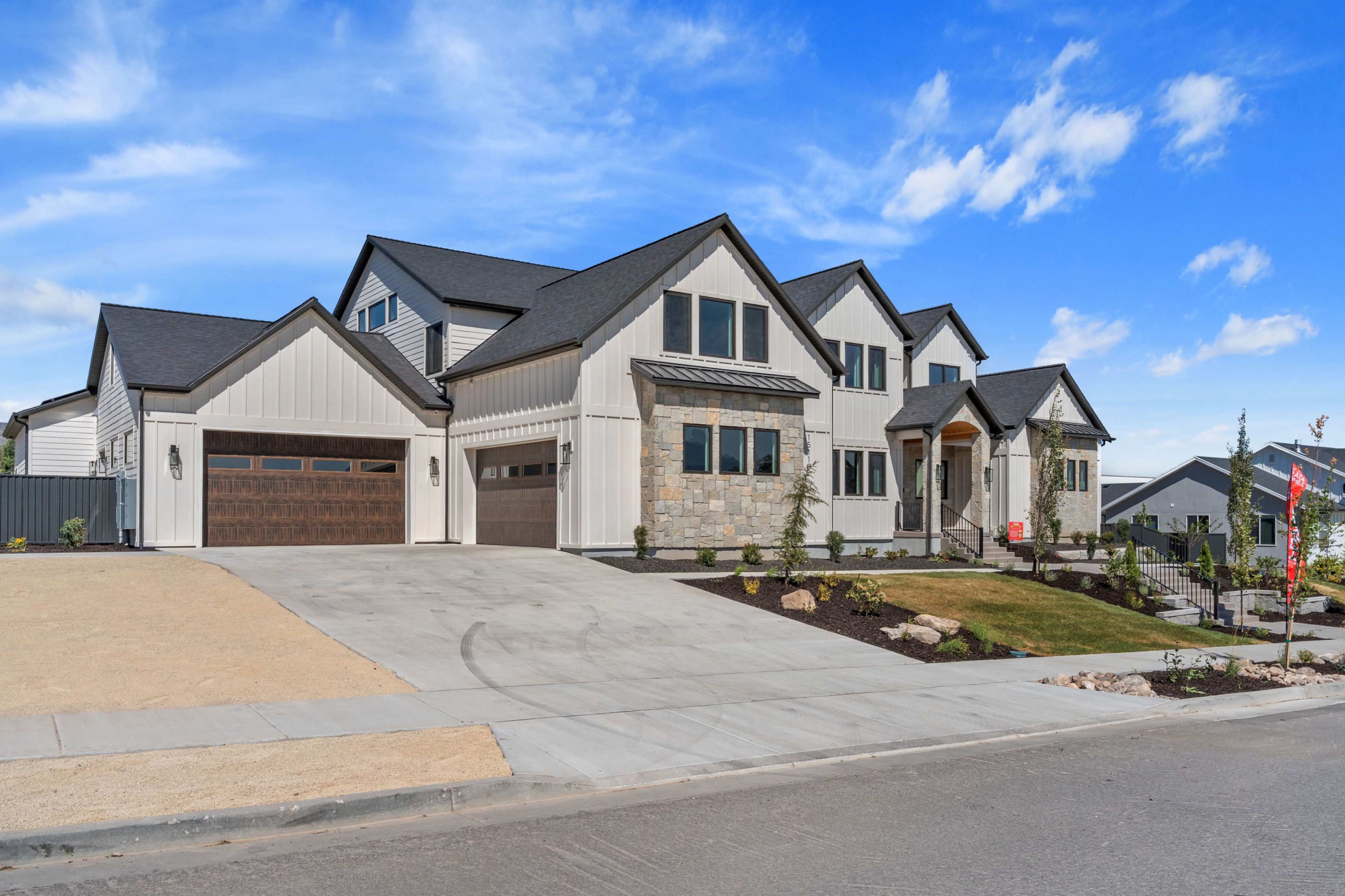 A large, modern house with a mix of stone and siding exteriors is positioned on a manicured lot with a paved driveway.